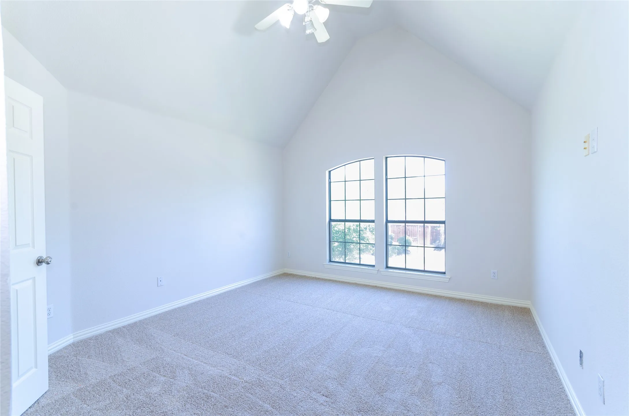 Bedroom # 4 Vaulted ceiling bedroom with arched divided light windows, ceiling fan, and light-colored carpeting