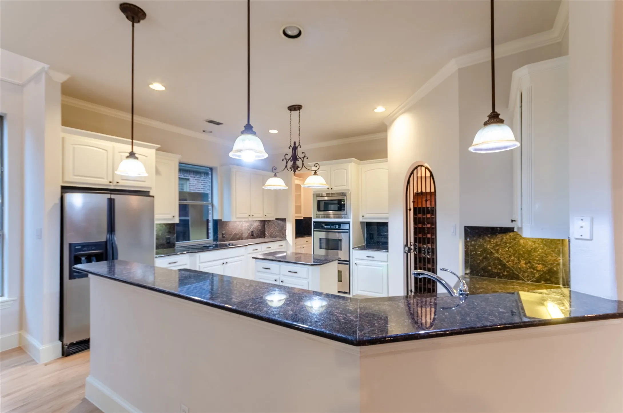 Spacious kitchen featuring white cabinetry, dark granite countertops with a matching backsplash, stainless steel appliances, and a central island