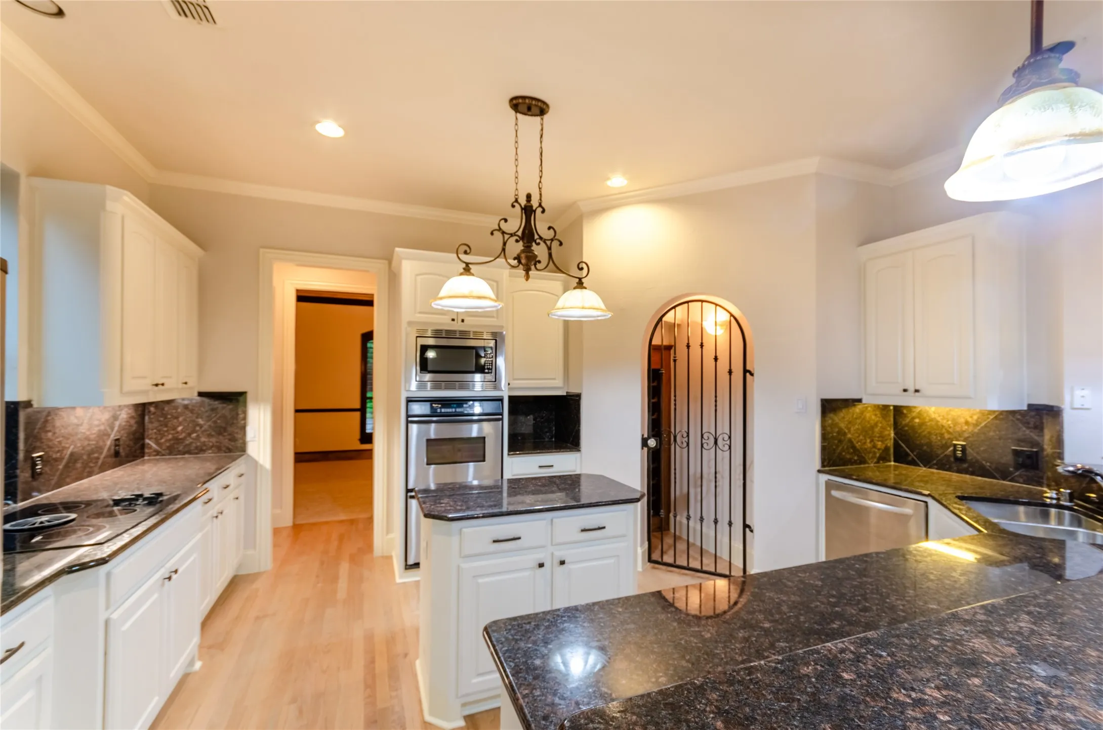 Kitchen featuring hardwood flooring, white cabinetry, dark stone countertops with matching backsplash, stainless steel appliances, and a central island with a pendant light fixture
