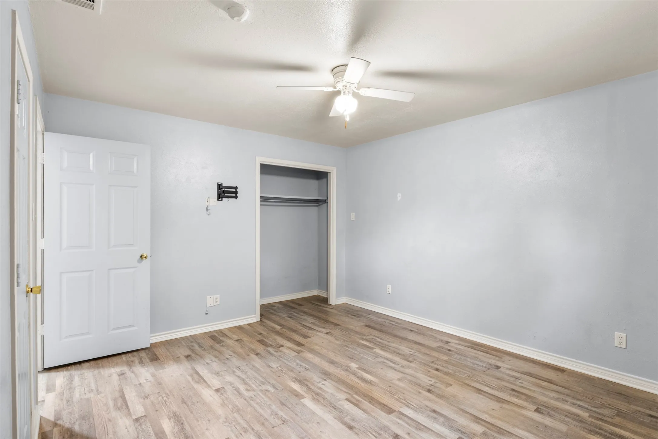 Room featuring wood-finish flooring, light blue walls, and a ceiling fan