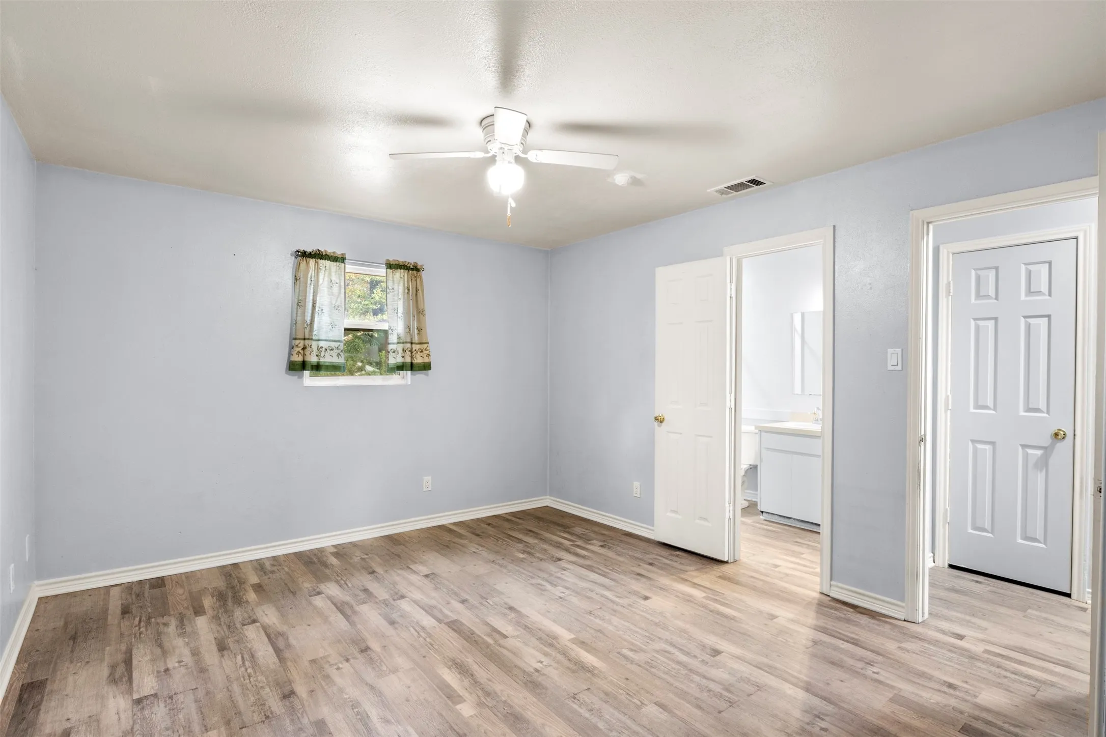 Spacious room featuring light wood-finish flooring and a ceiling fan with integrated lighting
