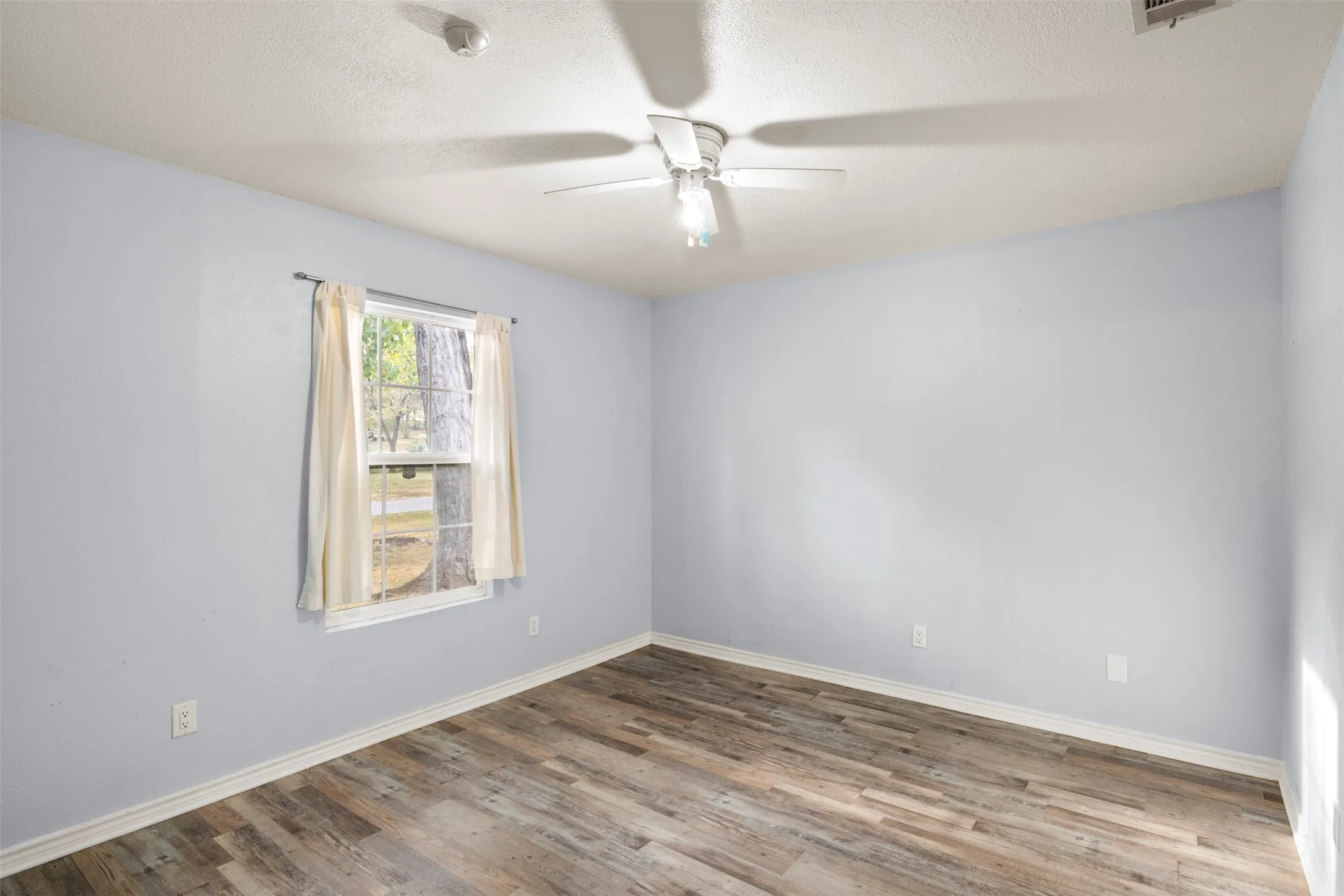 Spacious room featuring wood-finish flooring and a ceiling fan with integrated lighting