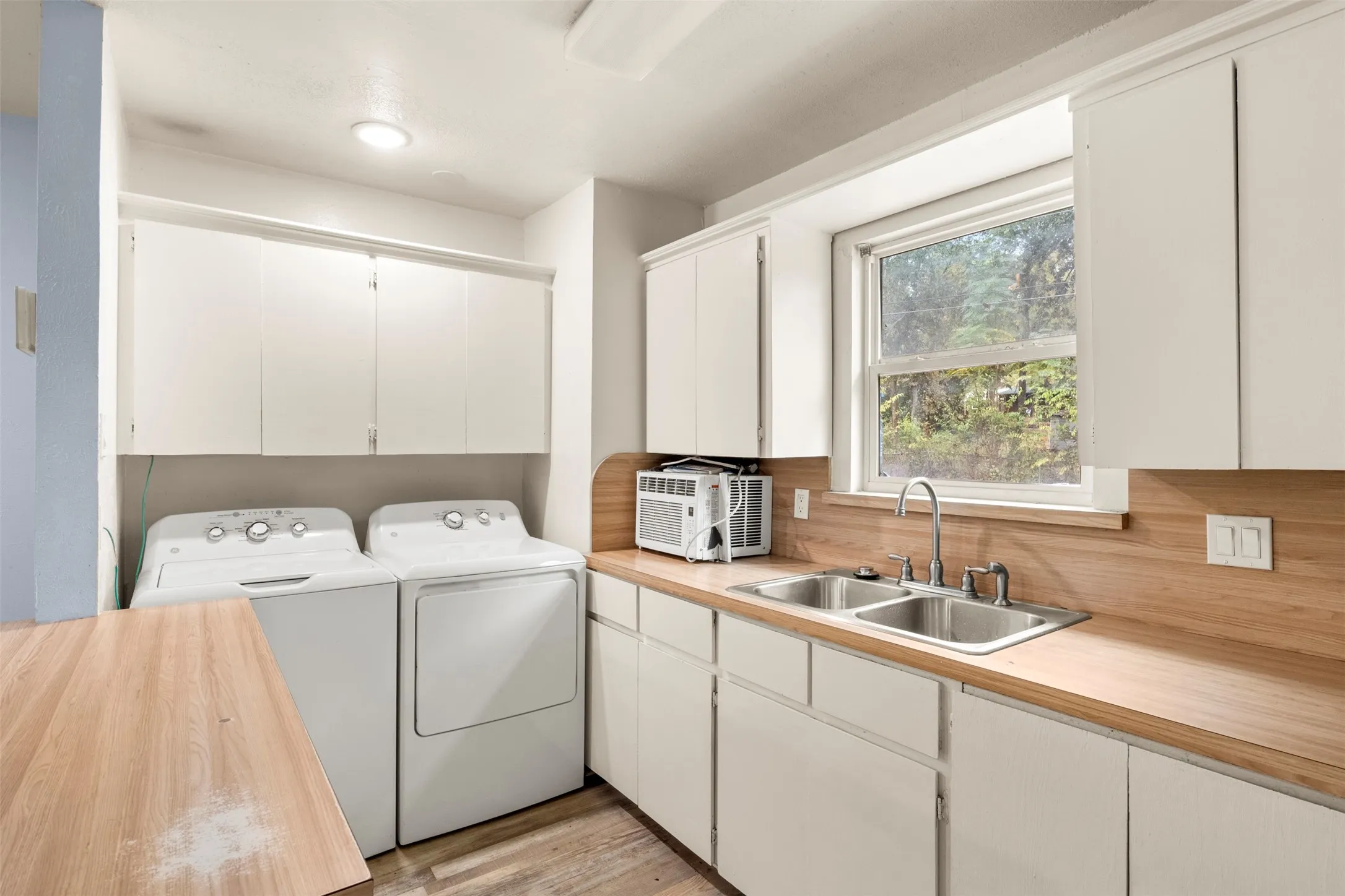 Utility area featuring white cabinetry, wood-finish countertops, and dual basin sink with a chrome faucet