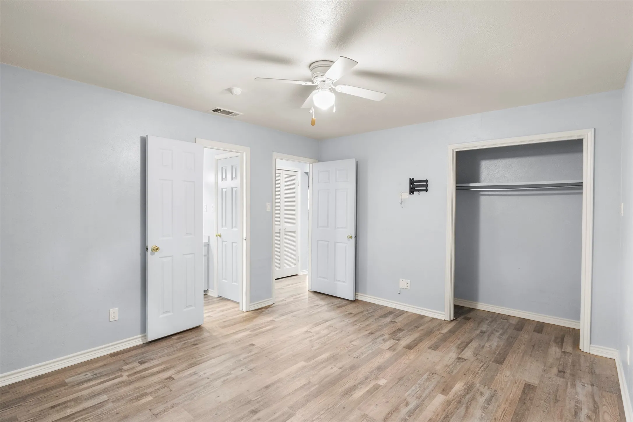 Spacious room featuring wood-finish flooring, light blue wall paint, and white trim