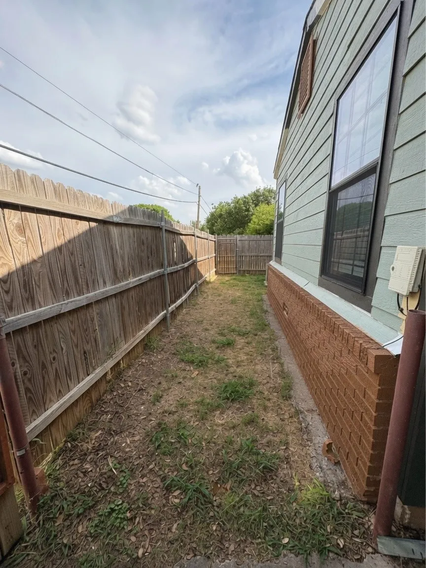 Side yard dog run with a wood privacy fence and a brick foundation