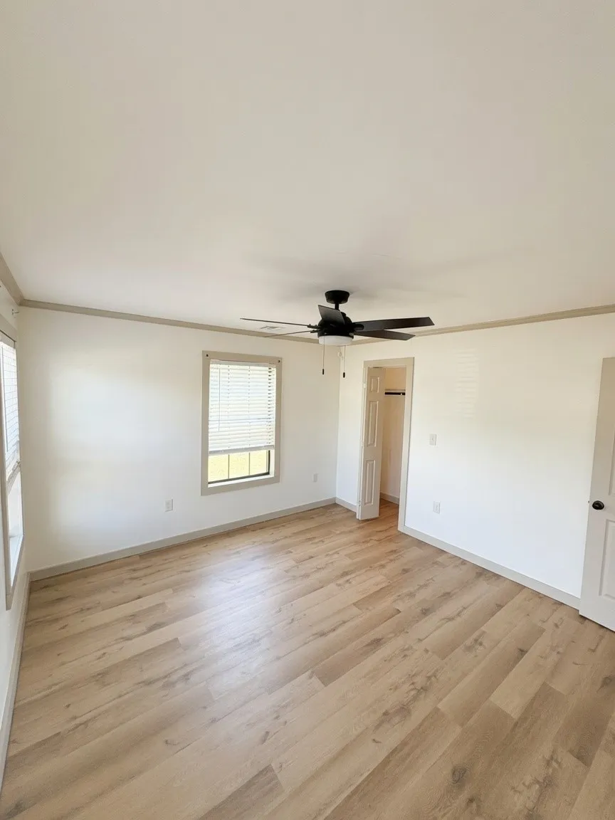 Spacious room featuring wood-finish flooring, white walls, and a black ceiling fan