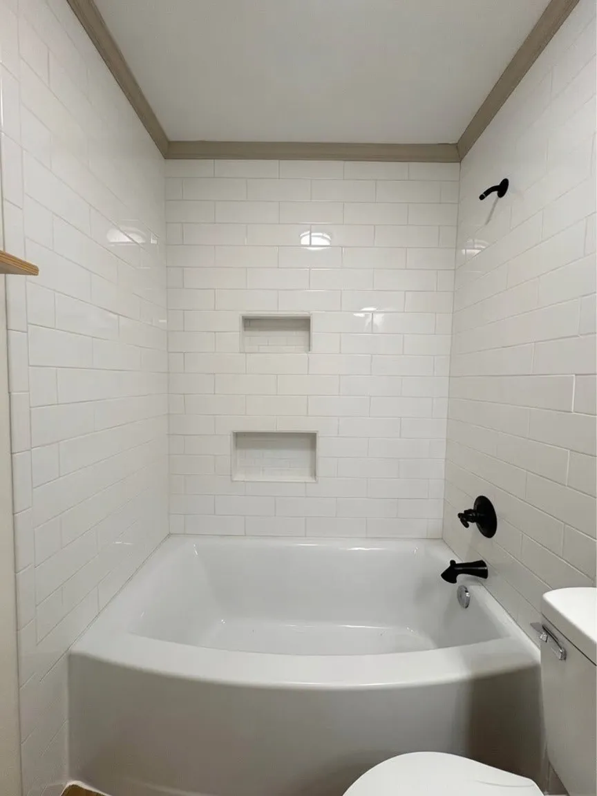Bathtub and shower combination featuring white subway tile surround, two built-in storage niches, and matte black fixtures