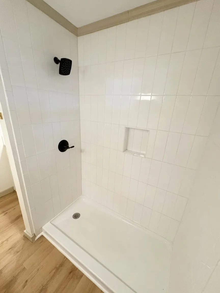 Shower featuring white subway tile walls, a built-in shower niche, matte black shower fixtures, and a white shower pan