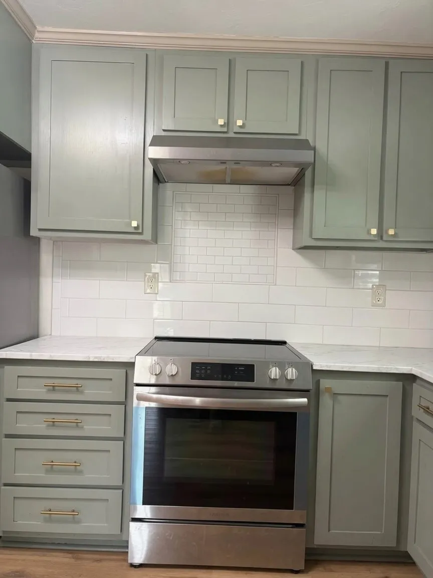 Kitchen featuring shaker-style cabinetry with gold-tone hardware, stainless steel range with matching hood, white subway tile backsplash, and light-toned countertops