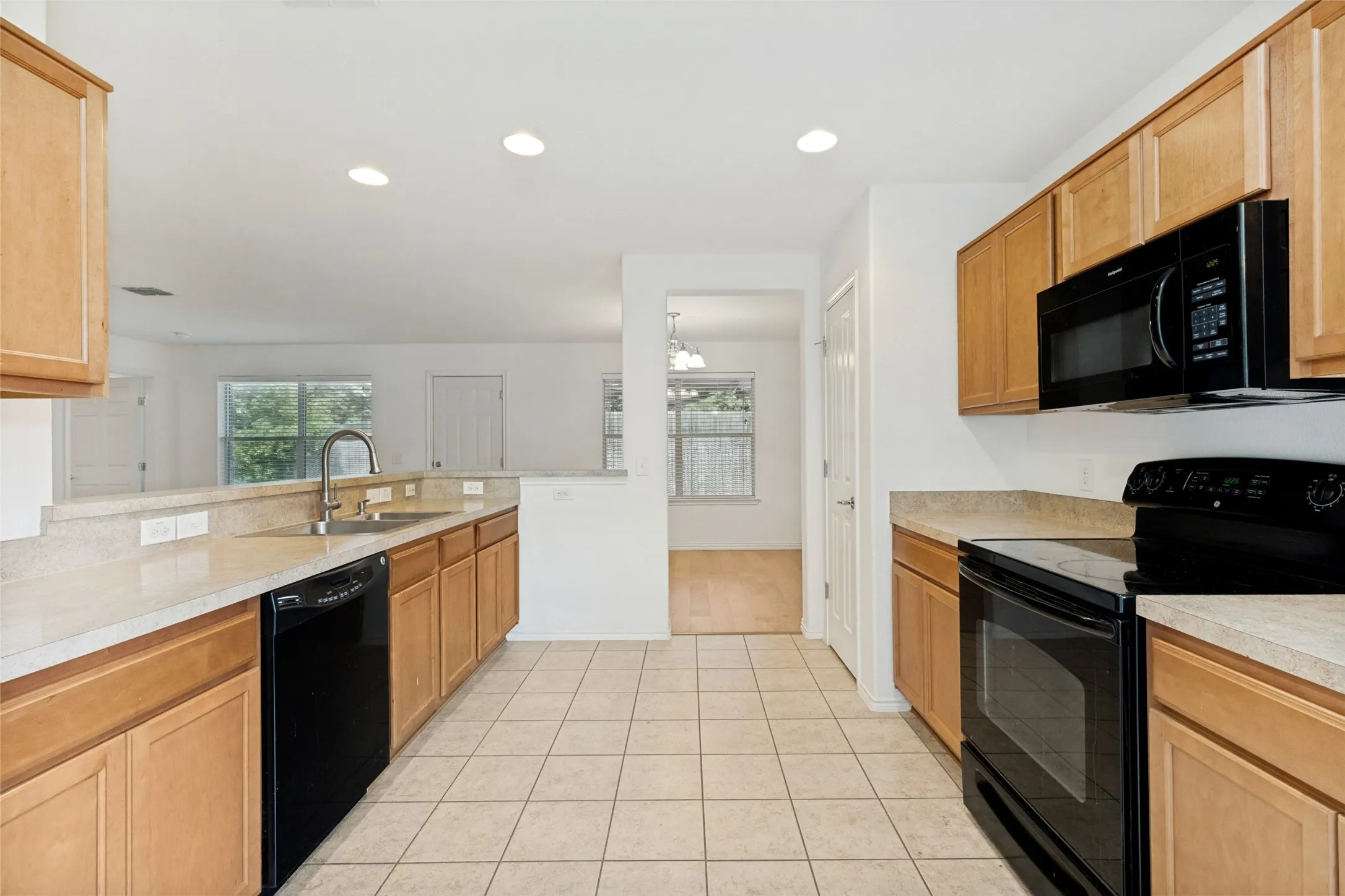 Kitchen featuring light wood cabinetry, light-toned countertops, ceramic tile flooring, and black appliances including a dishwasher, range, and microwave