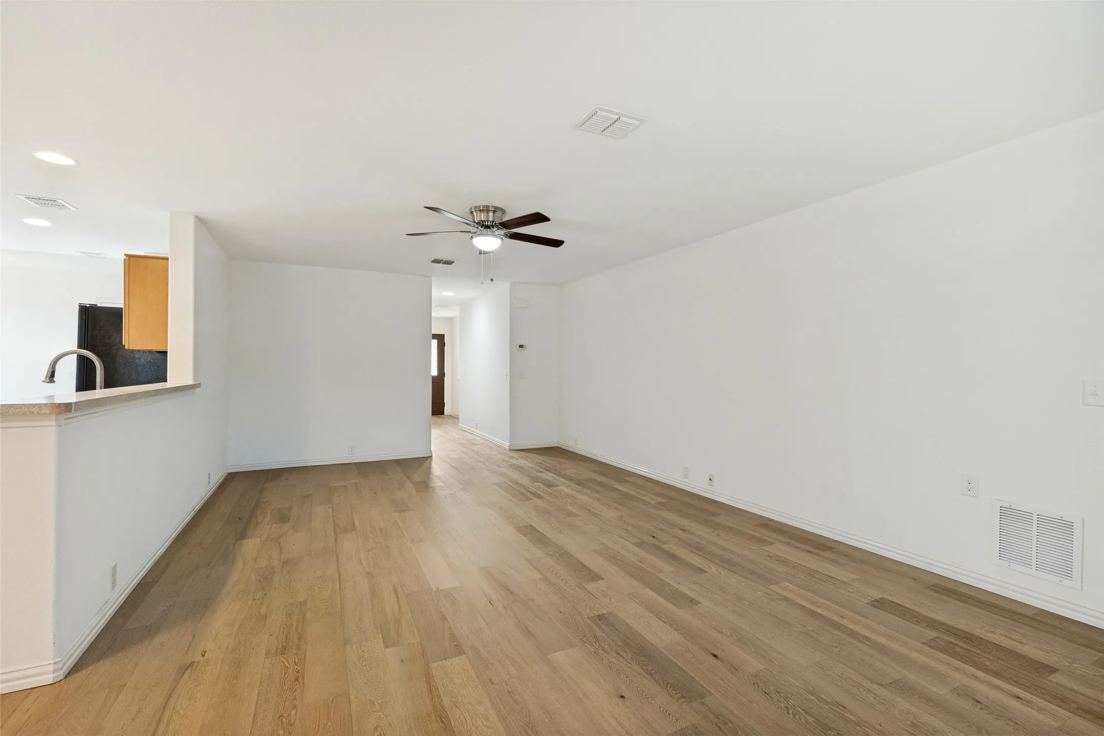 Expansive living area featuring light wood-finish flooring, a ceiling fan, and white painted walls