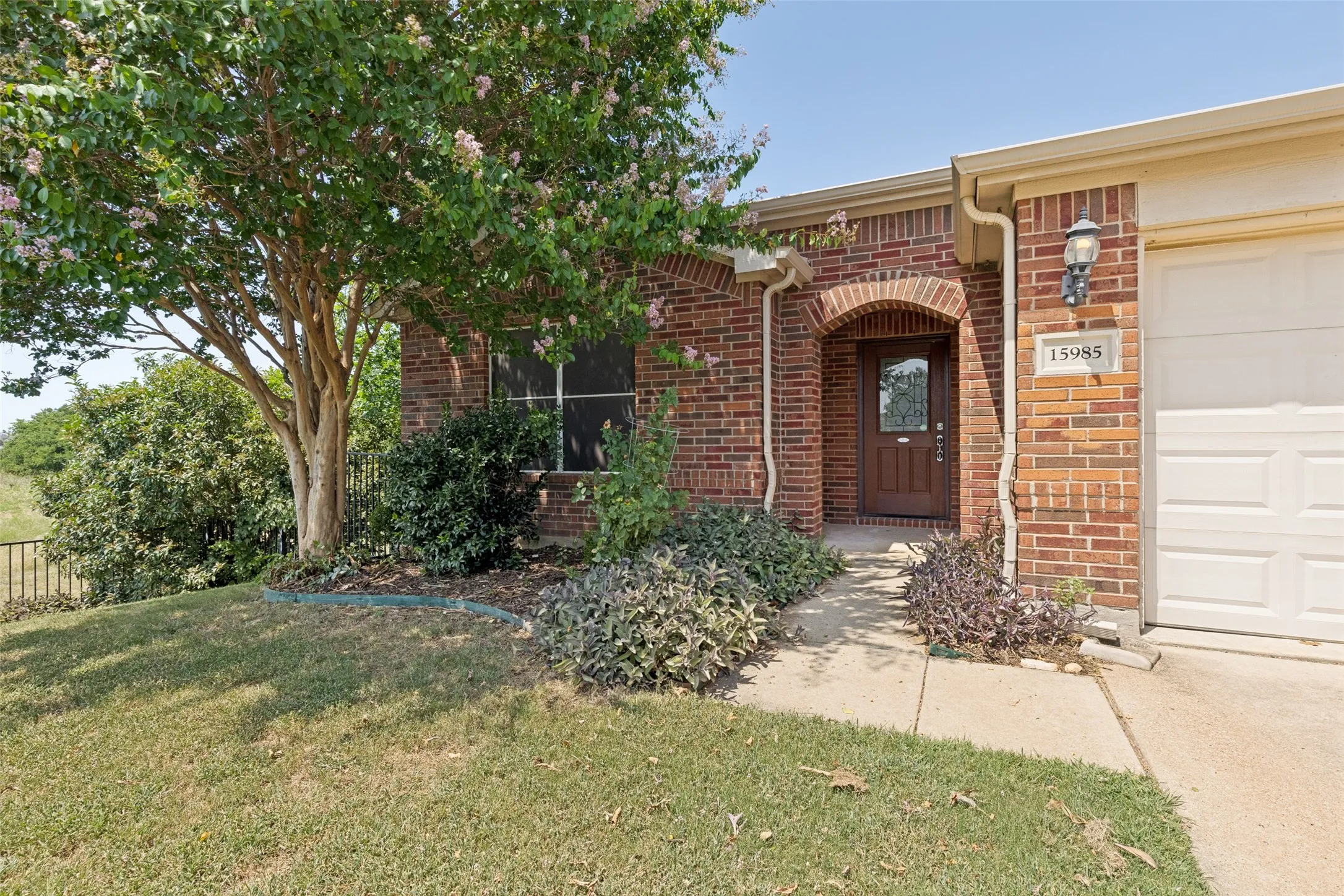 Brick exterior featuring an arched entryway, attached garage, and mature landscaping