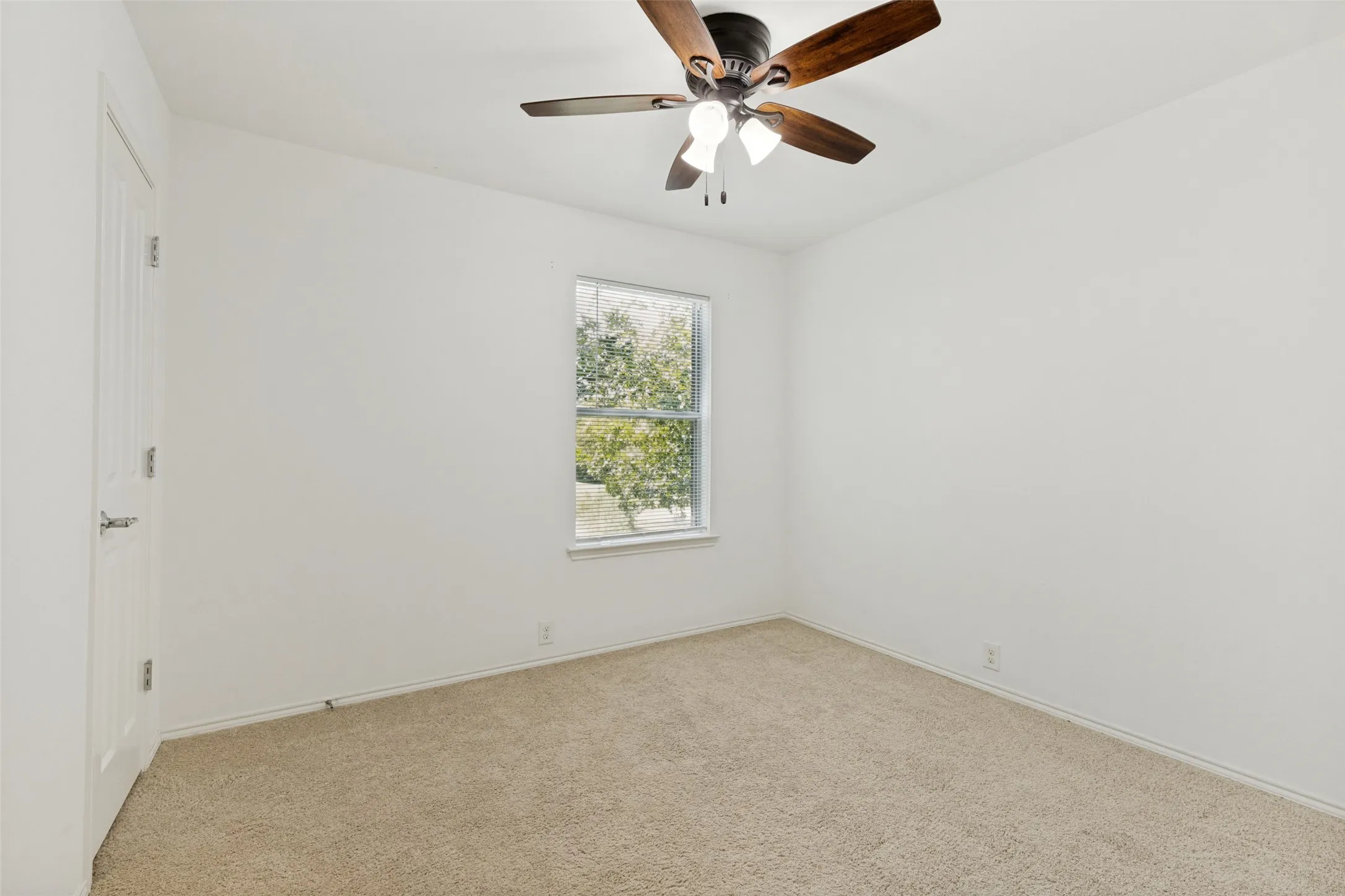 Spacious room featuring neutral carpeting, white walls, a multi-pane window with horizontal blinds, and a ceiling fan with integrated lighting