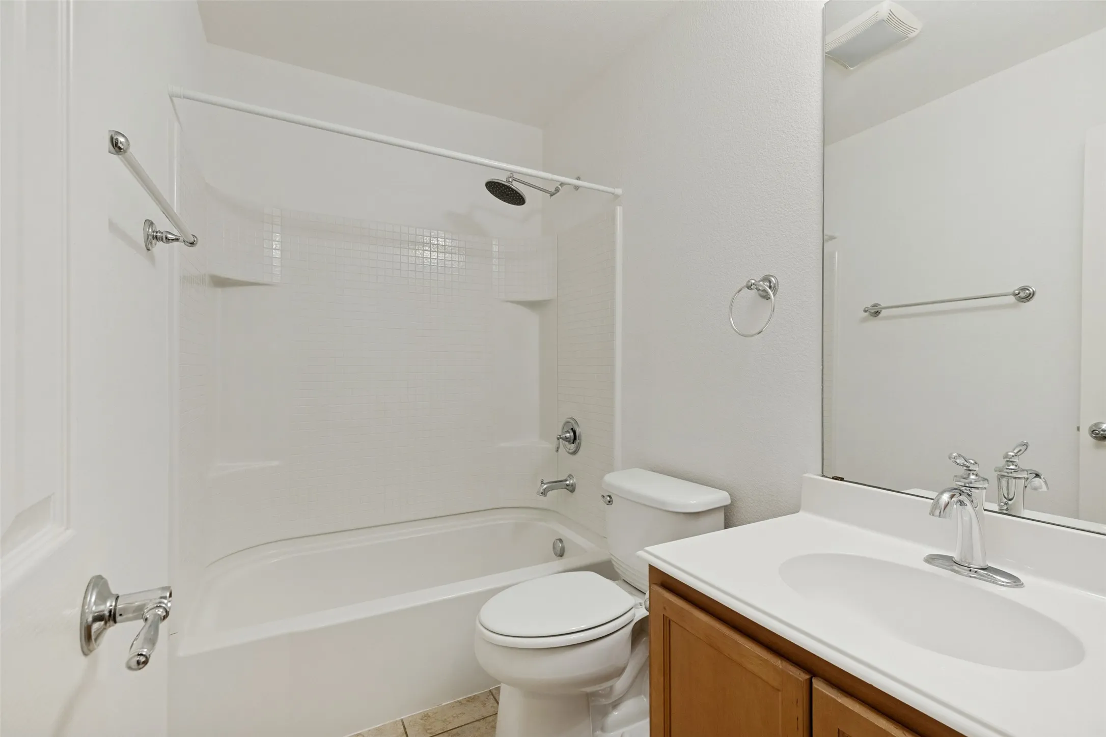 Bathroom featuring a bathtub with an integrated shower, white tile surround, and chrome fixtures