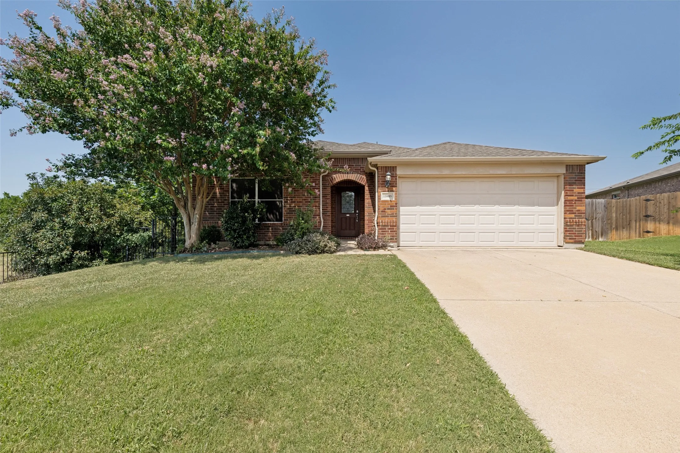 Brick exterior residence with an attached two-car garage, a concrete driveway, and a welcoming arched entry