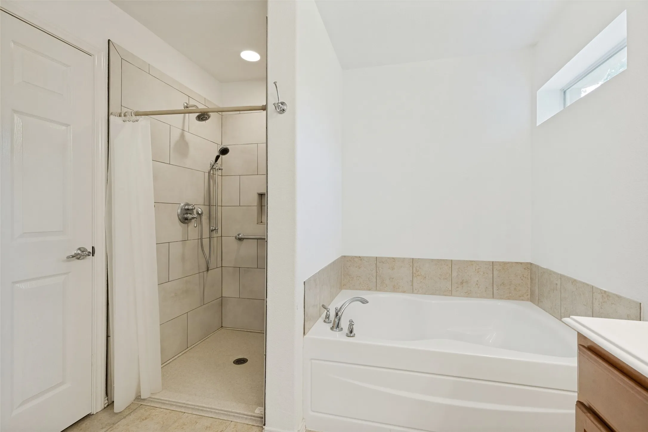 Bathroom featuring a walk-in shower with light-toned tile surround and a separate soaking tub with a tiled half-wall