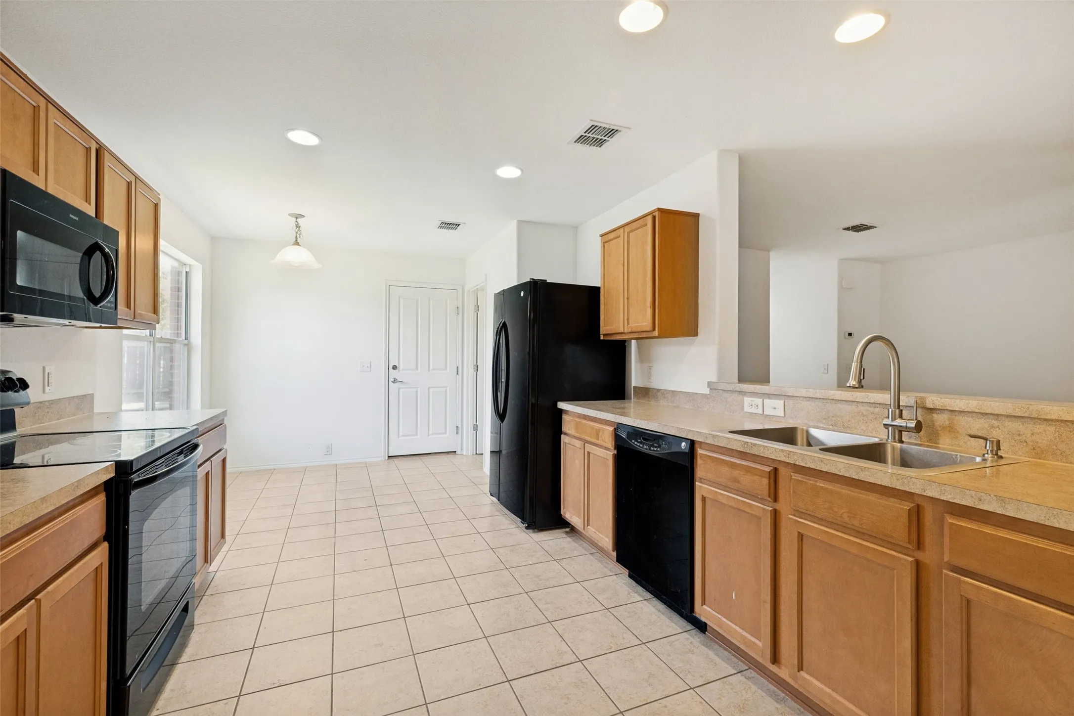 Kitchen featuring light wood-finish cabinetry, black appliances, light-toned countertops, and neutral tile flooring