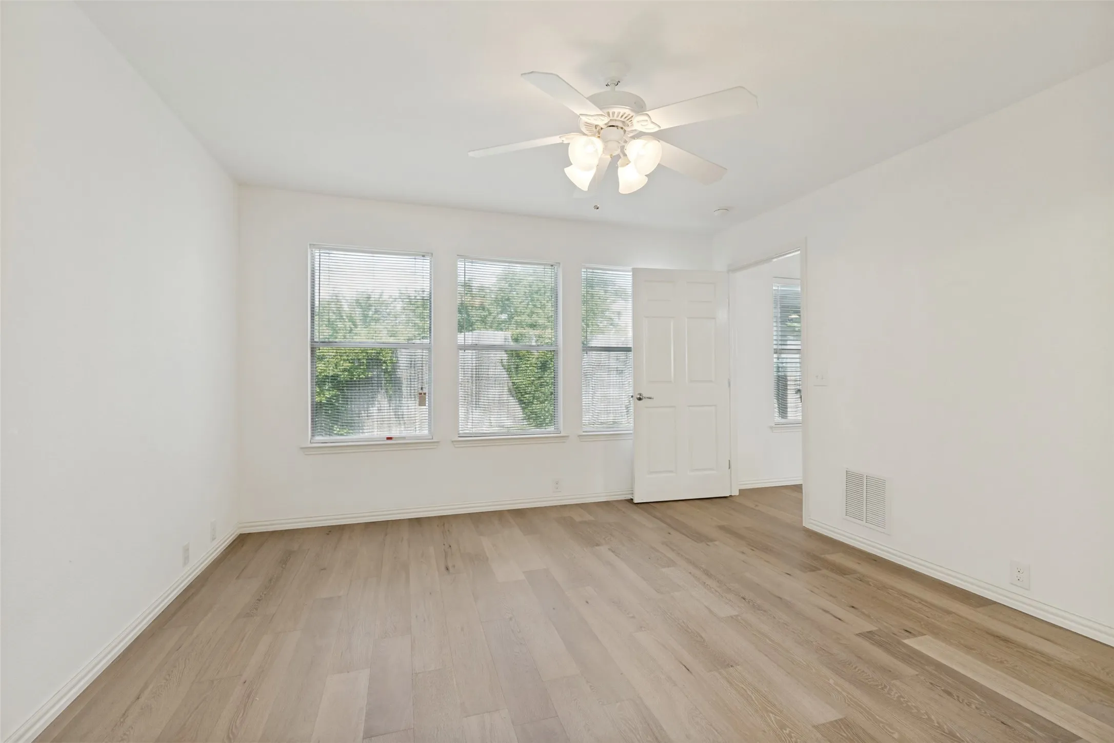Spacious room featuring light wood-finish flooring, white walls, and a ceiling fan with integrated lighting