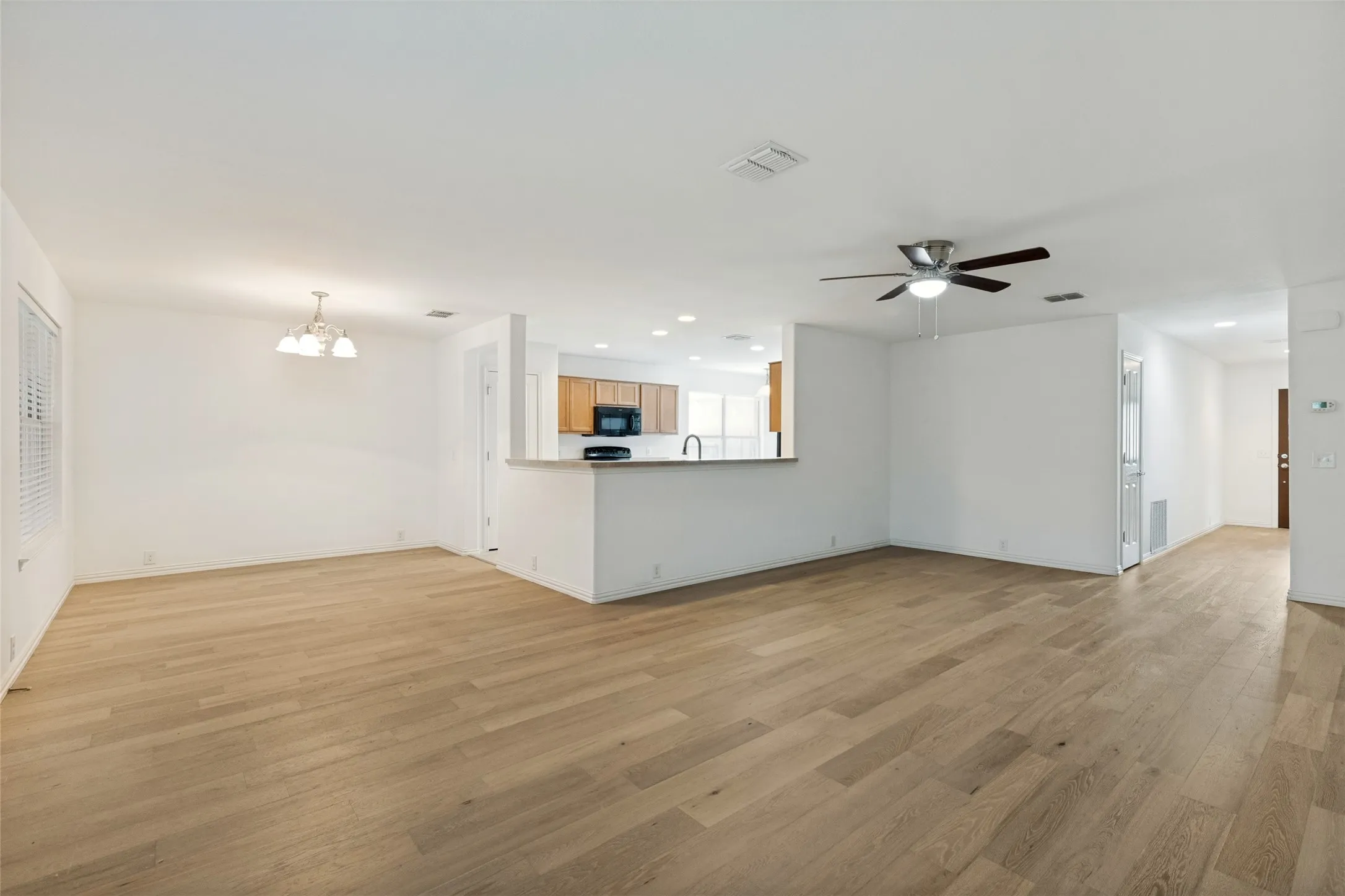 Expansive living area featuring light wood-finish flooring, a ceiling fan, and white painted walls