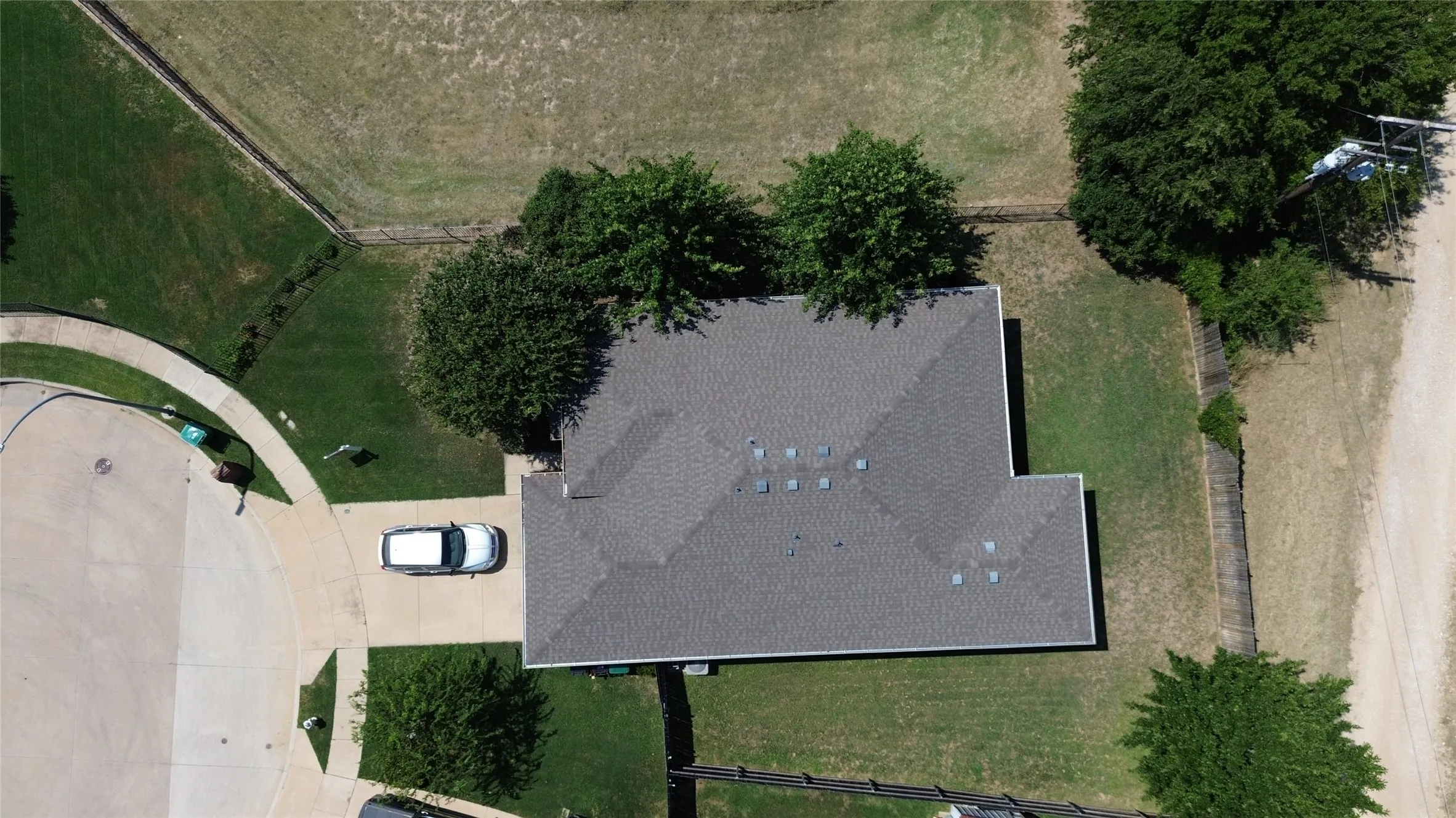 Aerial perspective showcasing property with a gray shingle roof, mature trees, and a concrete driveway