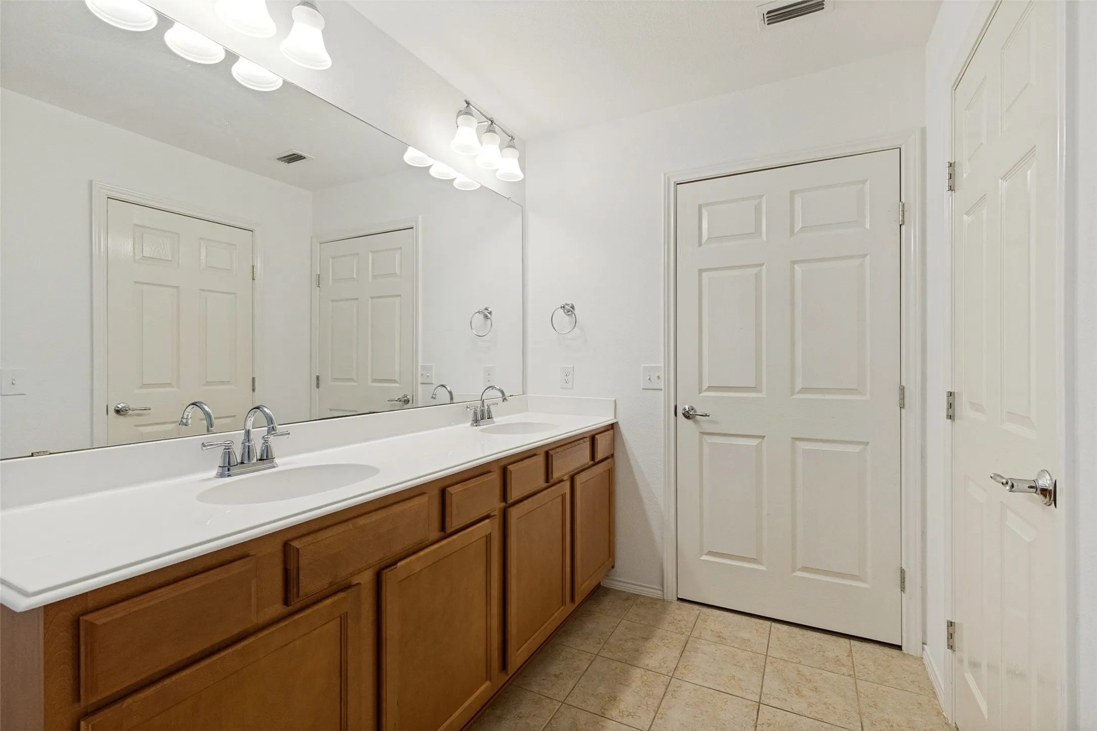 Bathroom featuring a dual vanity with wood cabinetry, white countertops, and chrome fixtures