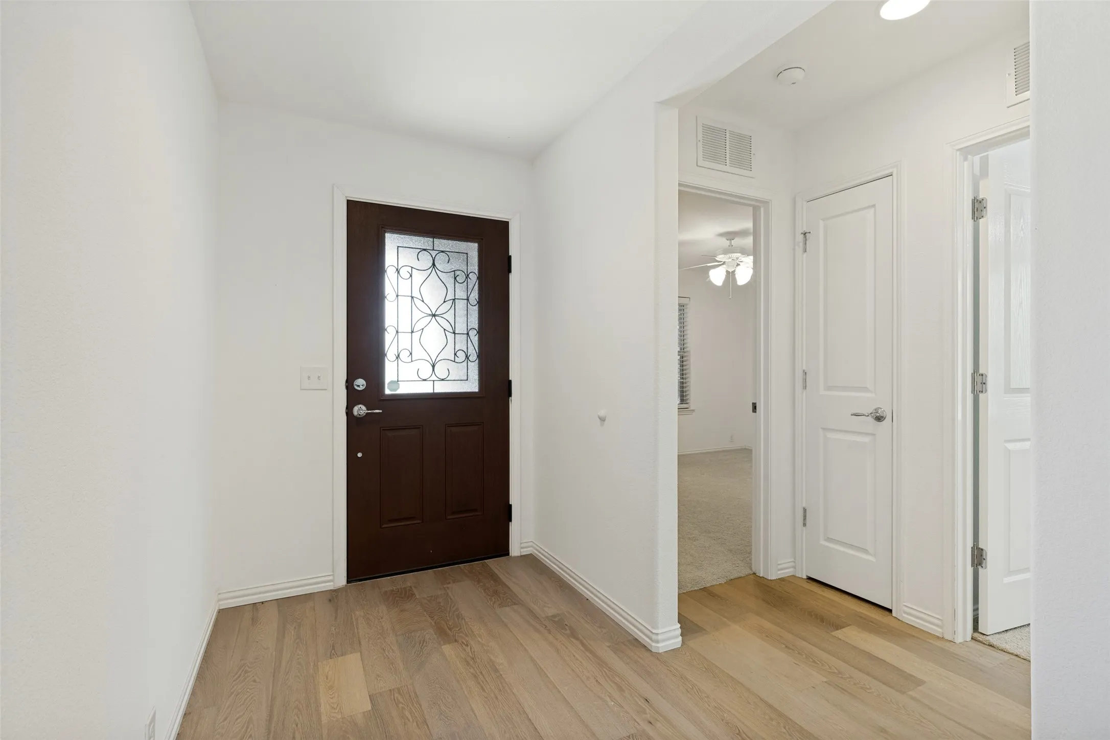 Entryway featuring a dark wood-finish door with decorative glass, wood-finish flooring, white trim, and light-colored walls