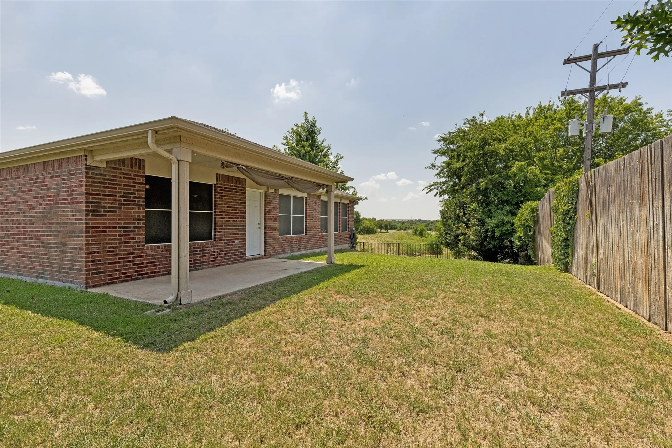 Rear exterior featuring a covered patio, brick facade, white door, and multiple windows