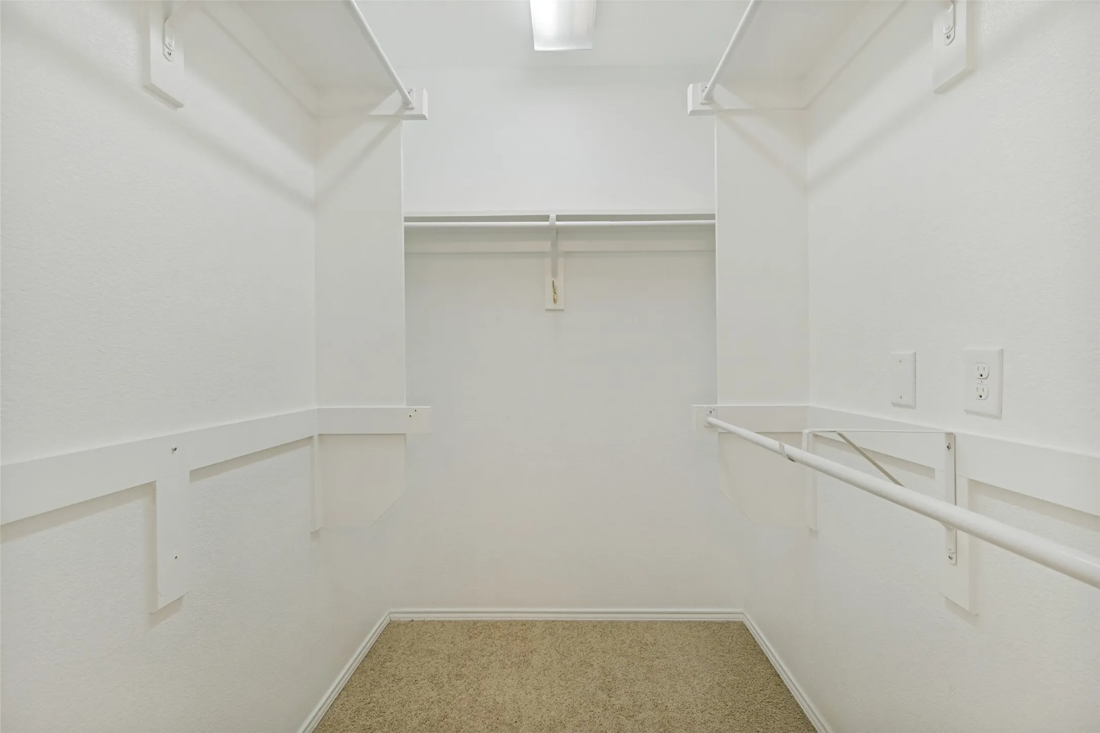 Primary walk-in closet featuring white walls, carpeting, and integrated shelving with hanging rods