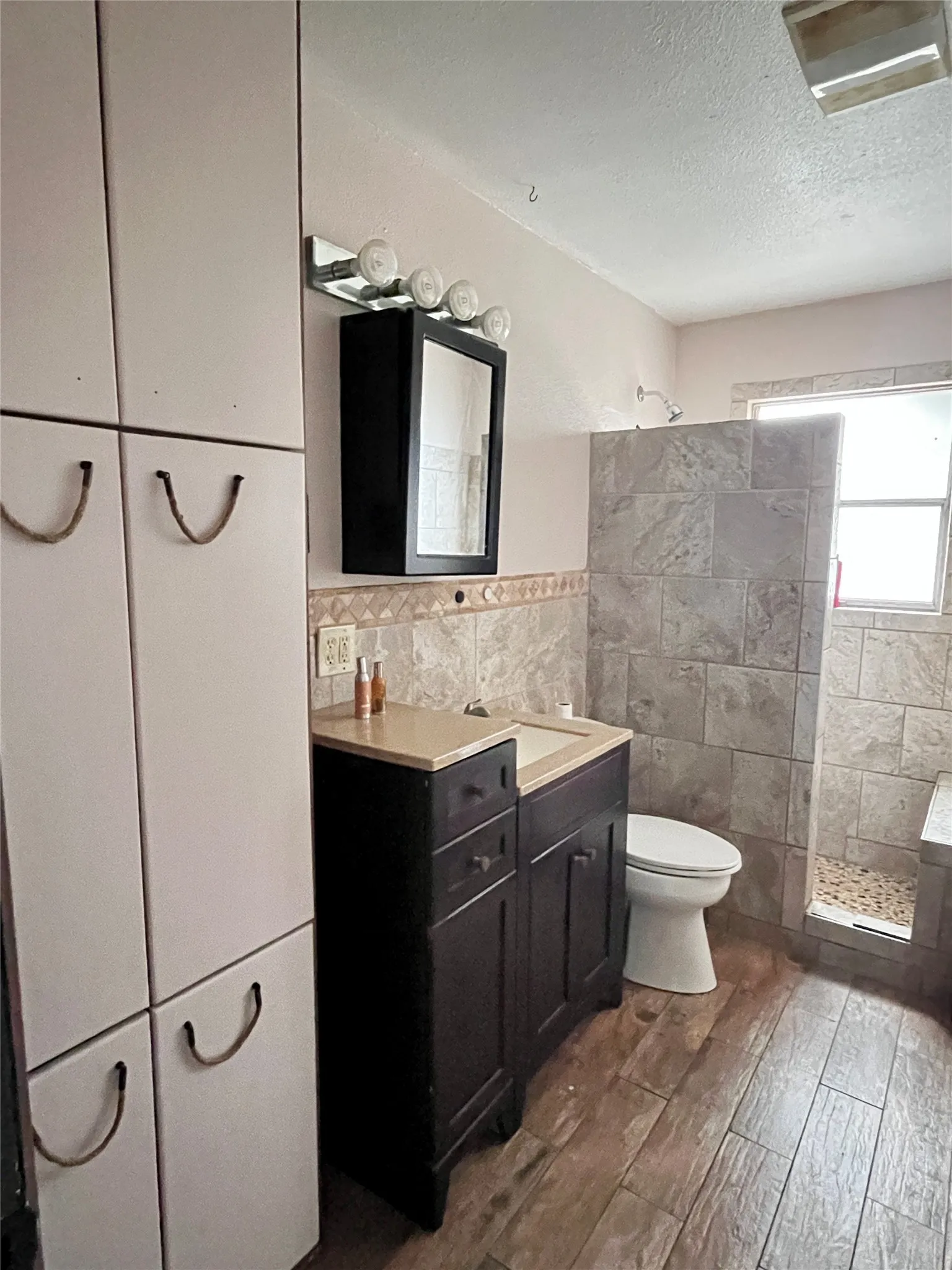 Updated restroom featuring a walk-in tile shower, modern vanity, and ample built-in storage.
