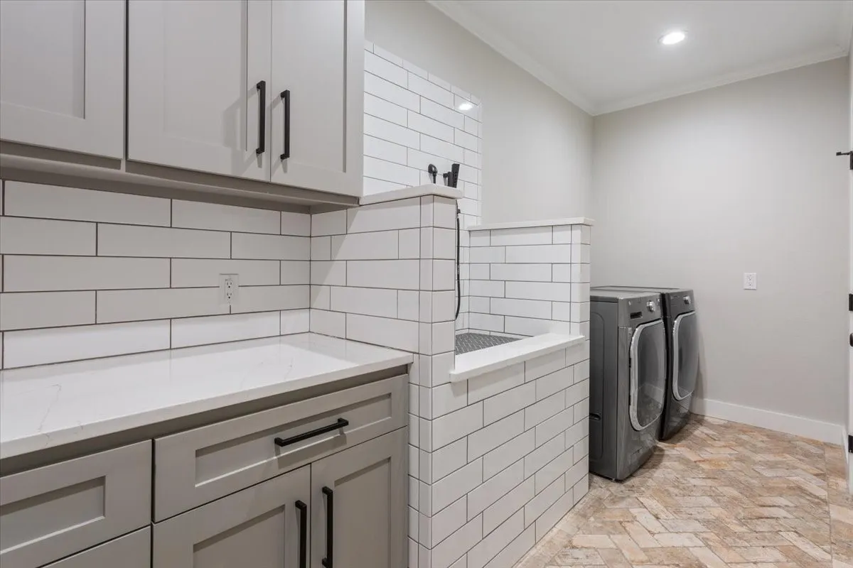 Laundry room featuring a tiled pet washing station, herringbone brick-style flooring, light gray cabinetry, solid surface countertops, and white subway tile backsplash