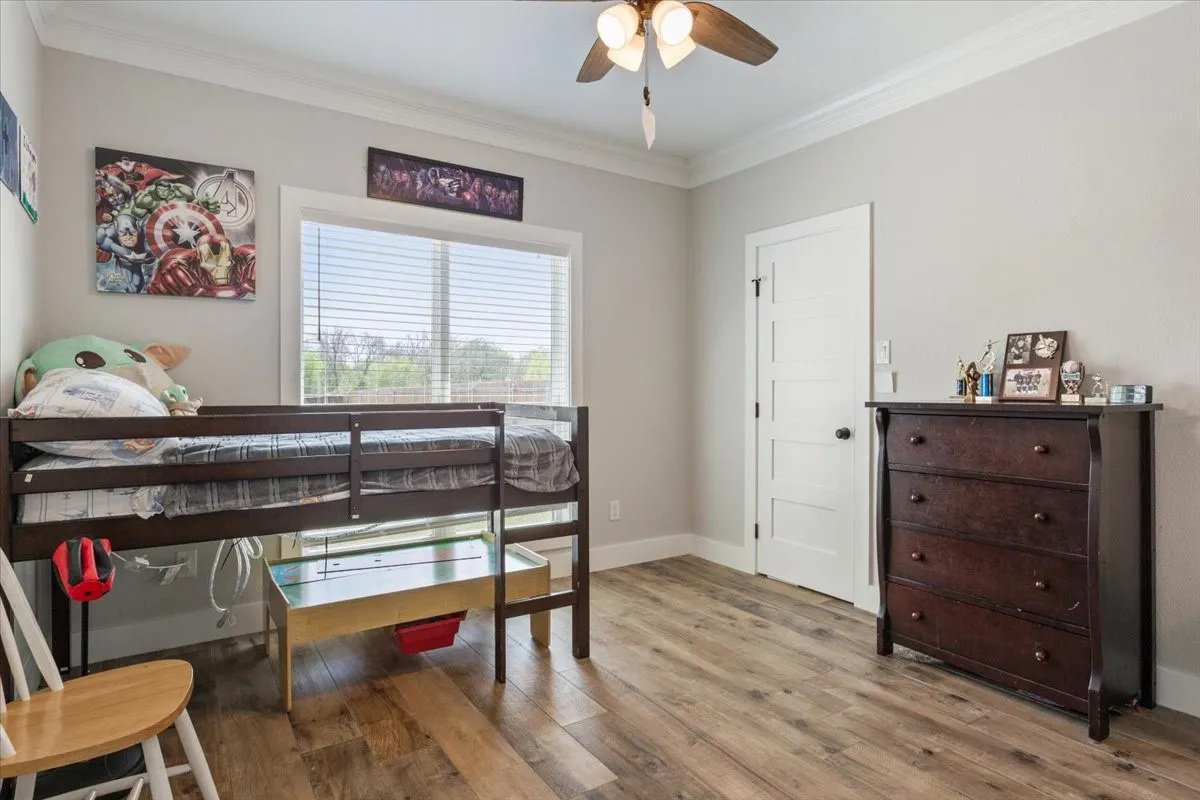 Spacious room featuring wood-finish flooring, a large window with horizontal blinds, and crown molding