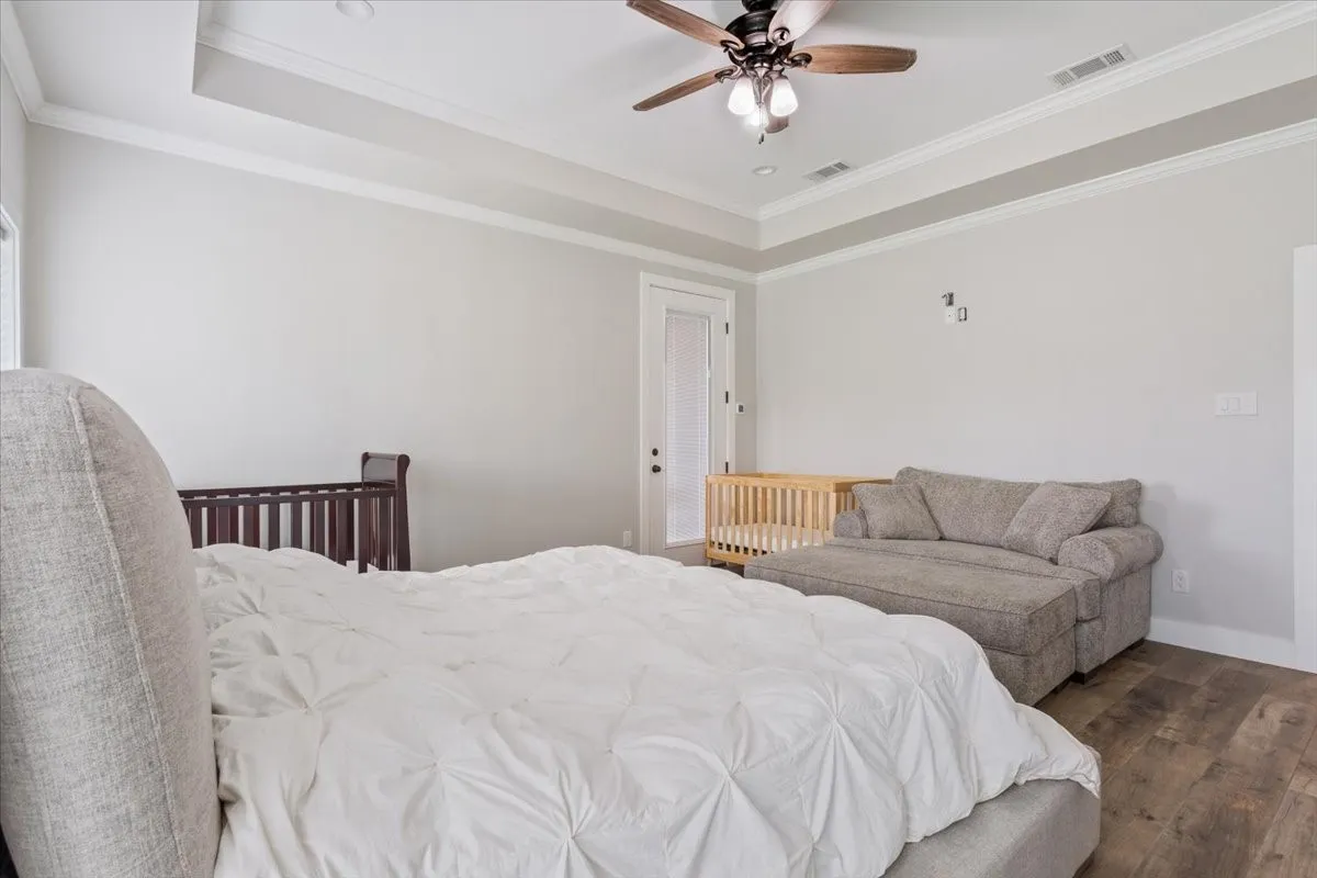 Spacious room featuring wood-finish flooring, a tray ceiling with crown molding, and a ceiling fan