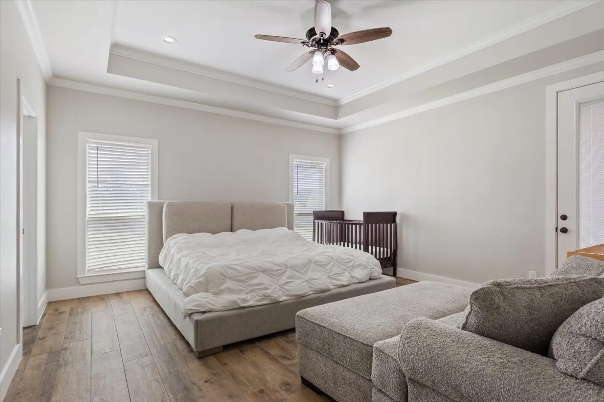 Spacious room featuring wood-finish flooring, a tray ceiling with recessed lighting, crown molding, and a ceiling fan