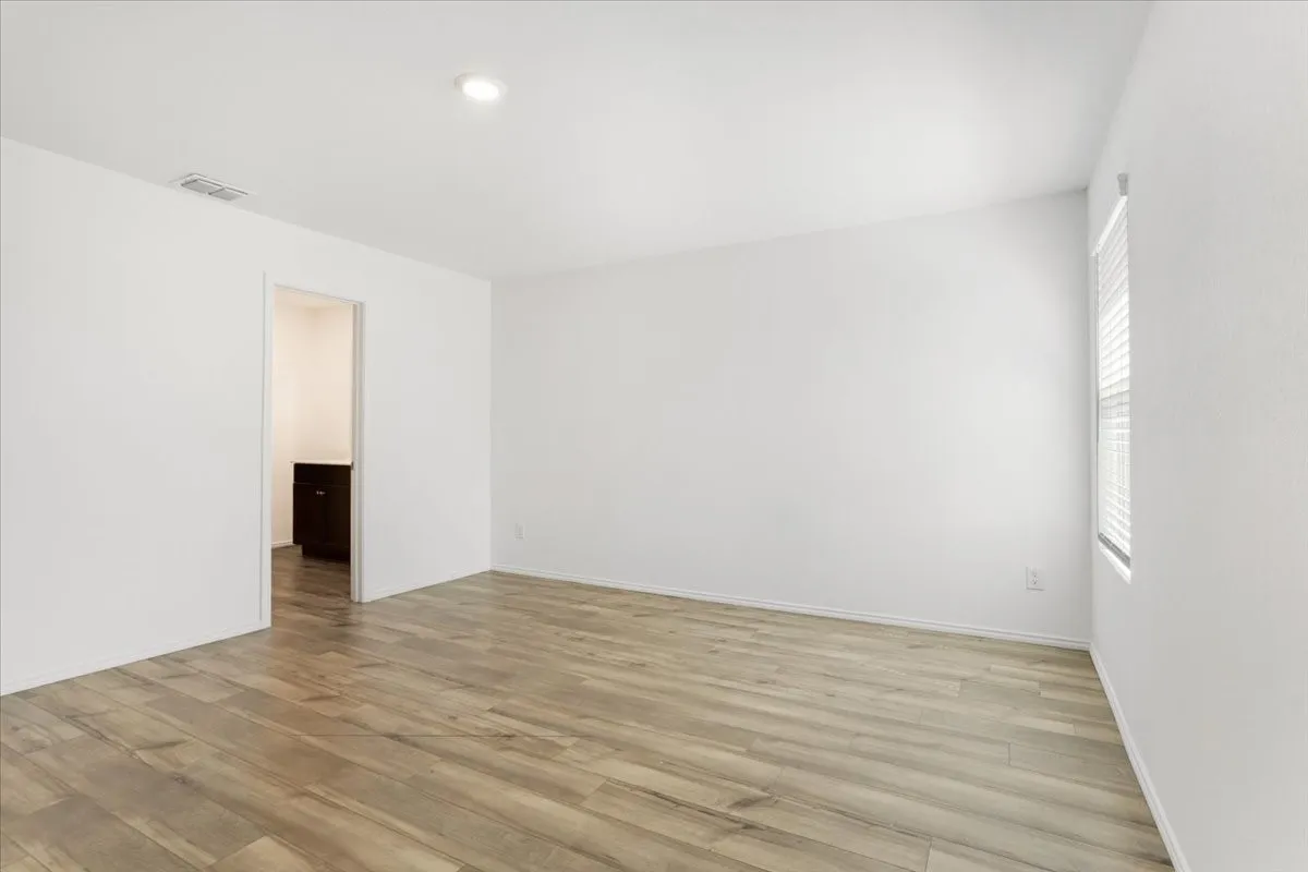 Spacious room featuring wood-finish flooring, white walls, recessed lighting, and natural light from a window