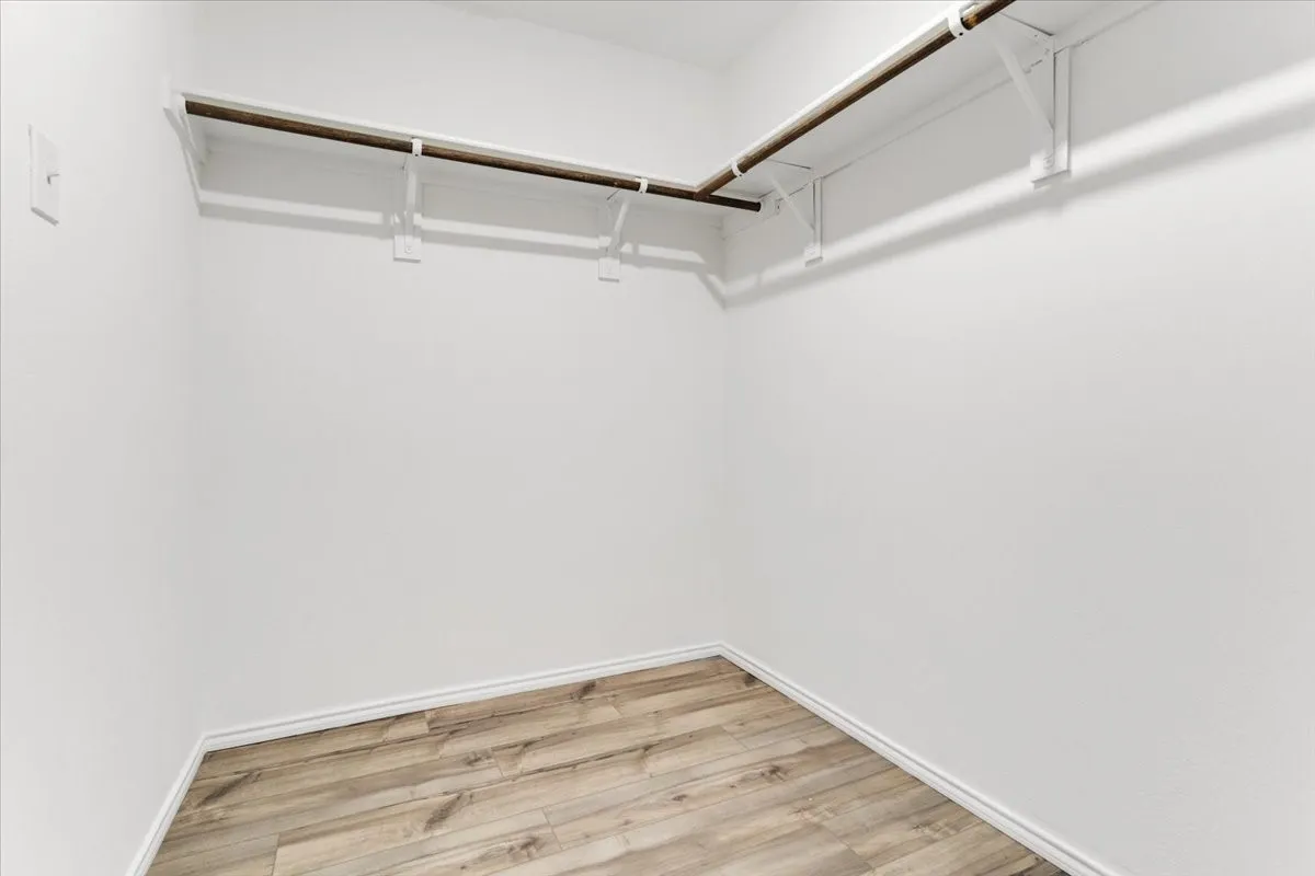 Spacious walk-in closet featuring polished wood-finish flooring, white drywall construction, and dual clothing rods with hanging hardware for maximum storage capacity