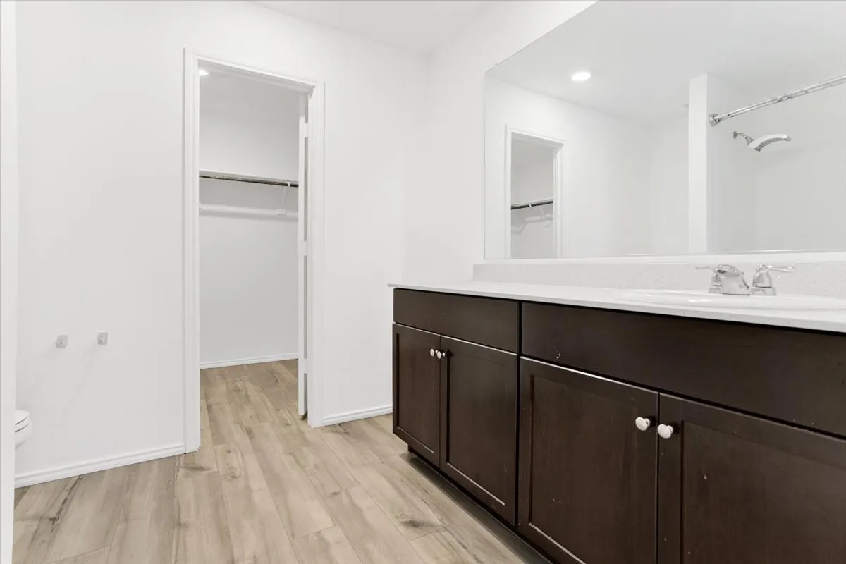 Spa-inspired primary bathroom showcasing a dark wood vanity with dual sinks, white quartz countertop, polished chrome hardware, and an expansive framed mirror