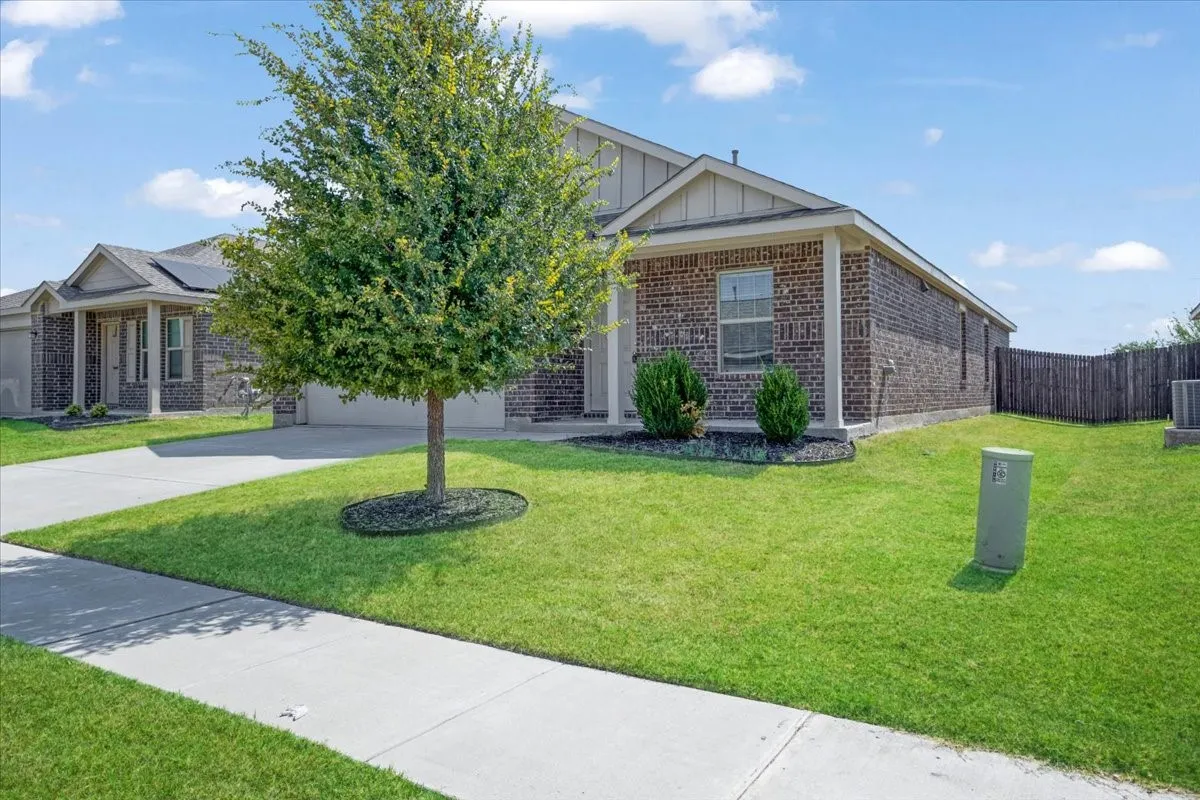 Charming brick home situated on a spacious landscaped lot featuring a mature shade tree, manicured lawn, and concrete driveway