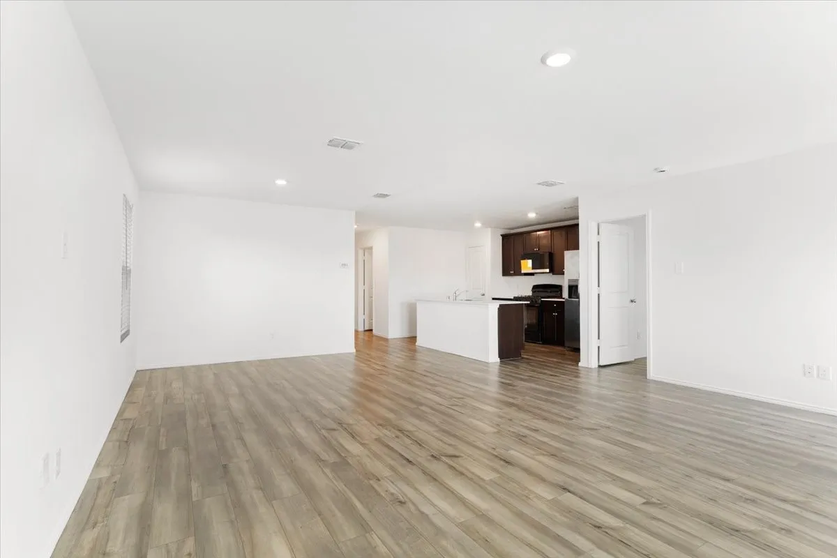 Open-concept living space featuring expansive wood-finish flooring, recessed ceiling lighting, and white painted walls