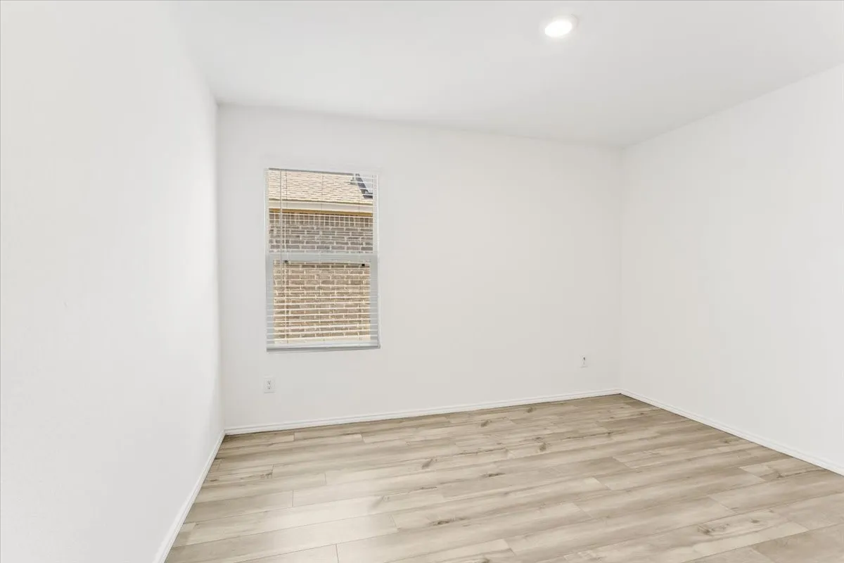 Bright, light-filled bedroom showcasing pristine white walls, recessed ceiling lighting, and warm wood-finish flooring throughout