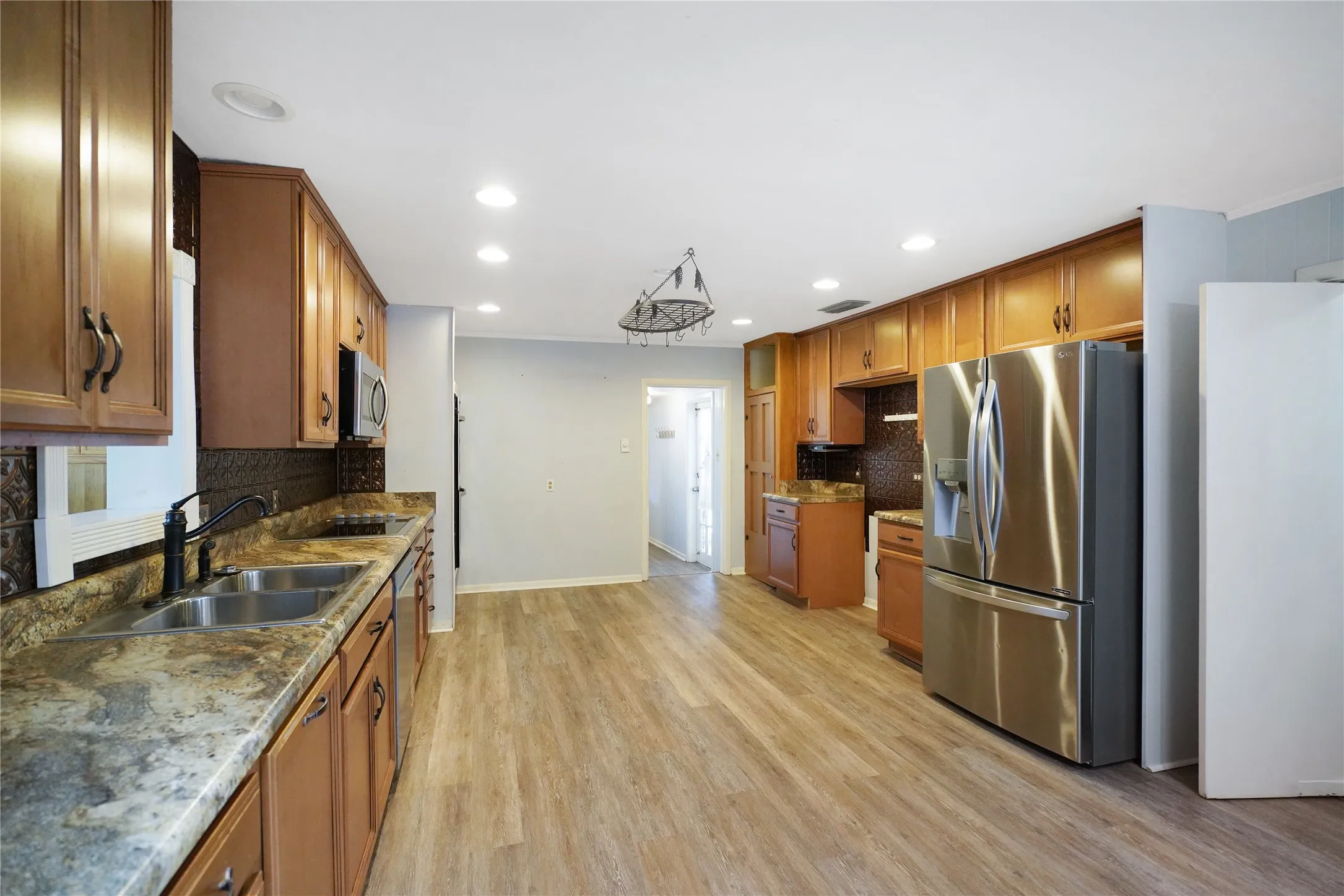 Spacious kitchen featuring extensive wood cabinetry, granite-patterned countertops, stainless steel appliances, and wood-finish flooring