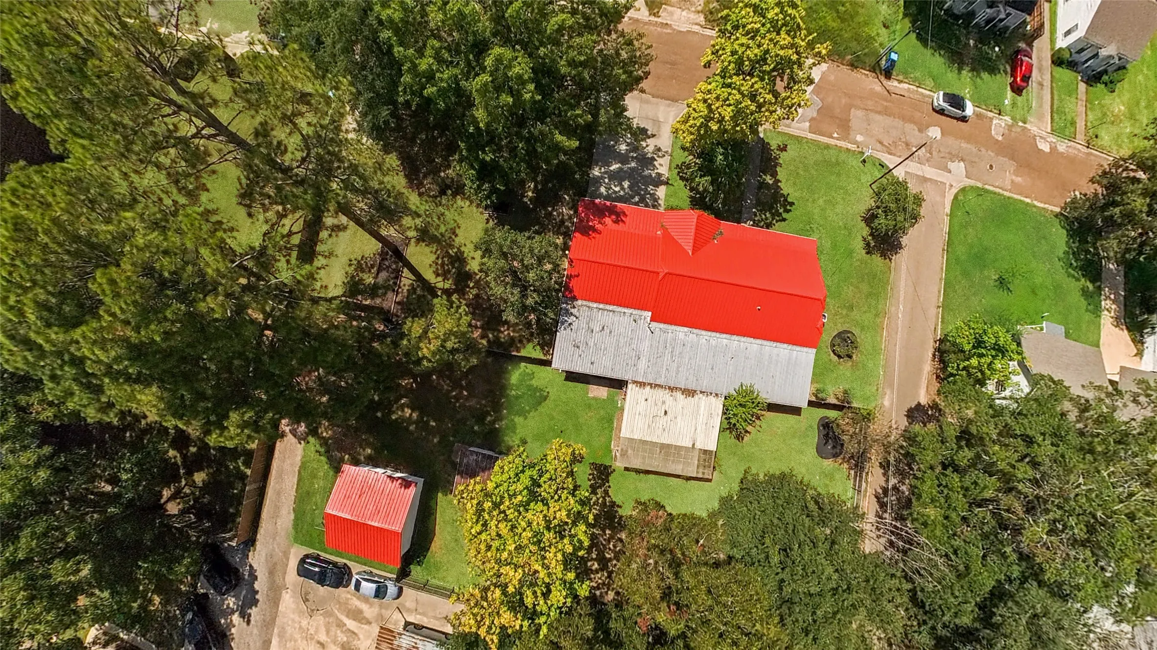 Red metal roof, expansive green lawn, mature trees, paved driveways, secondary red-roofed structure