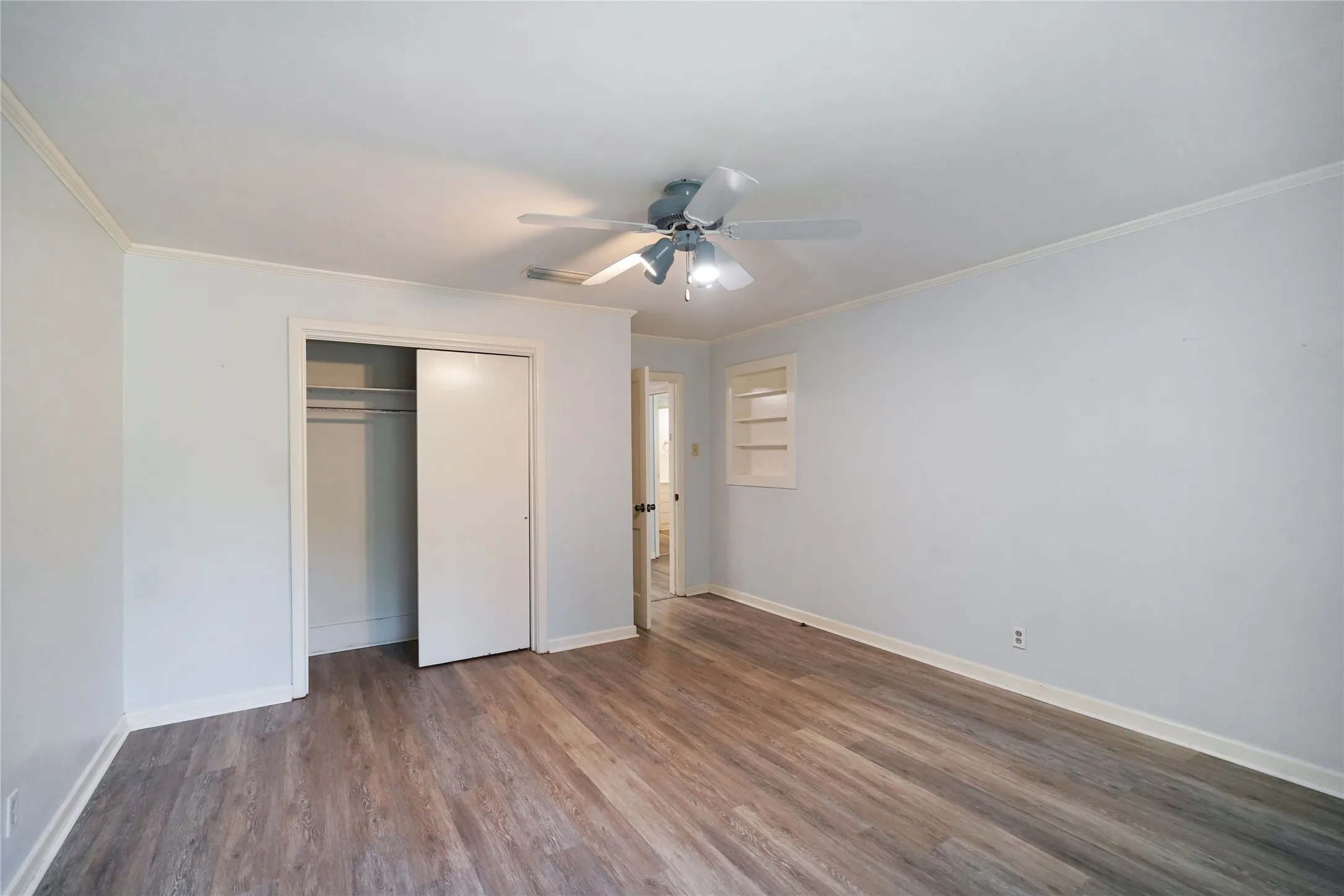 Spacious room featuring wood-finish flooring, a ceiling fan, sliding closet doors, and built-in shelving