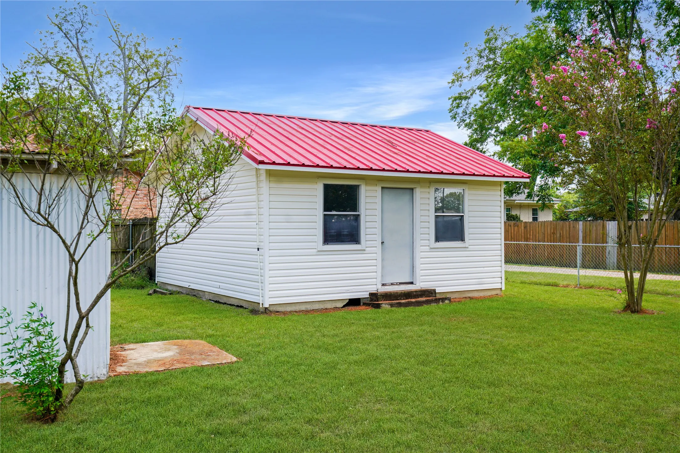 White vinyl siding building featuring a red metal roof and two single-pane windows