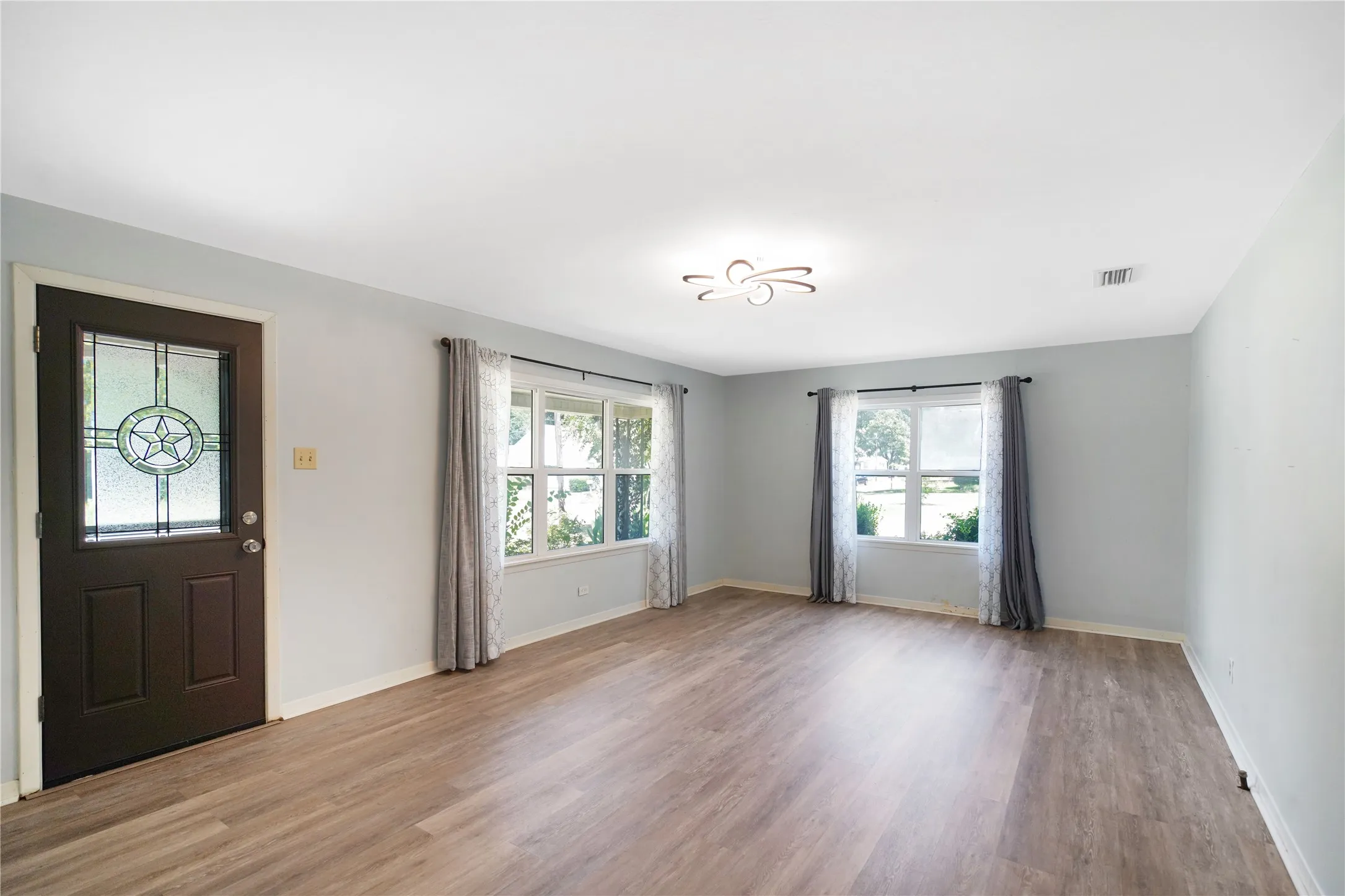 Bright living area featuring wood-finish flooring, light blue wall paint, and multiple windows
