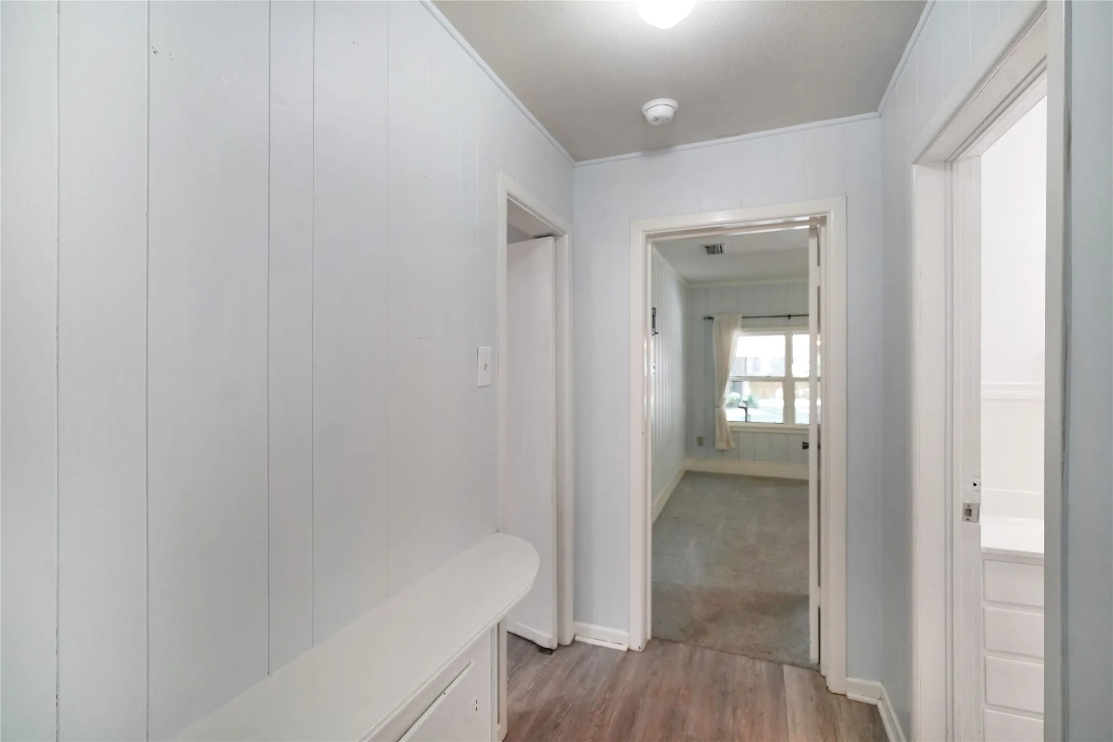Hallway featuring light wood-finish flooring and vertical paneled walls