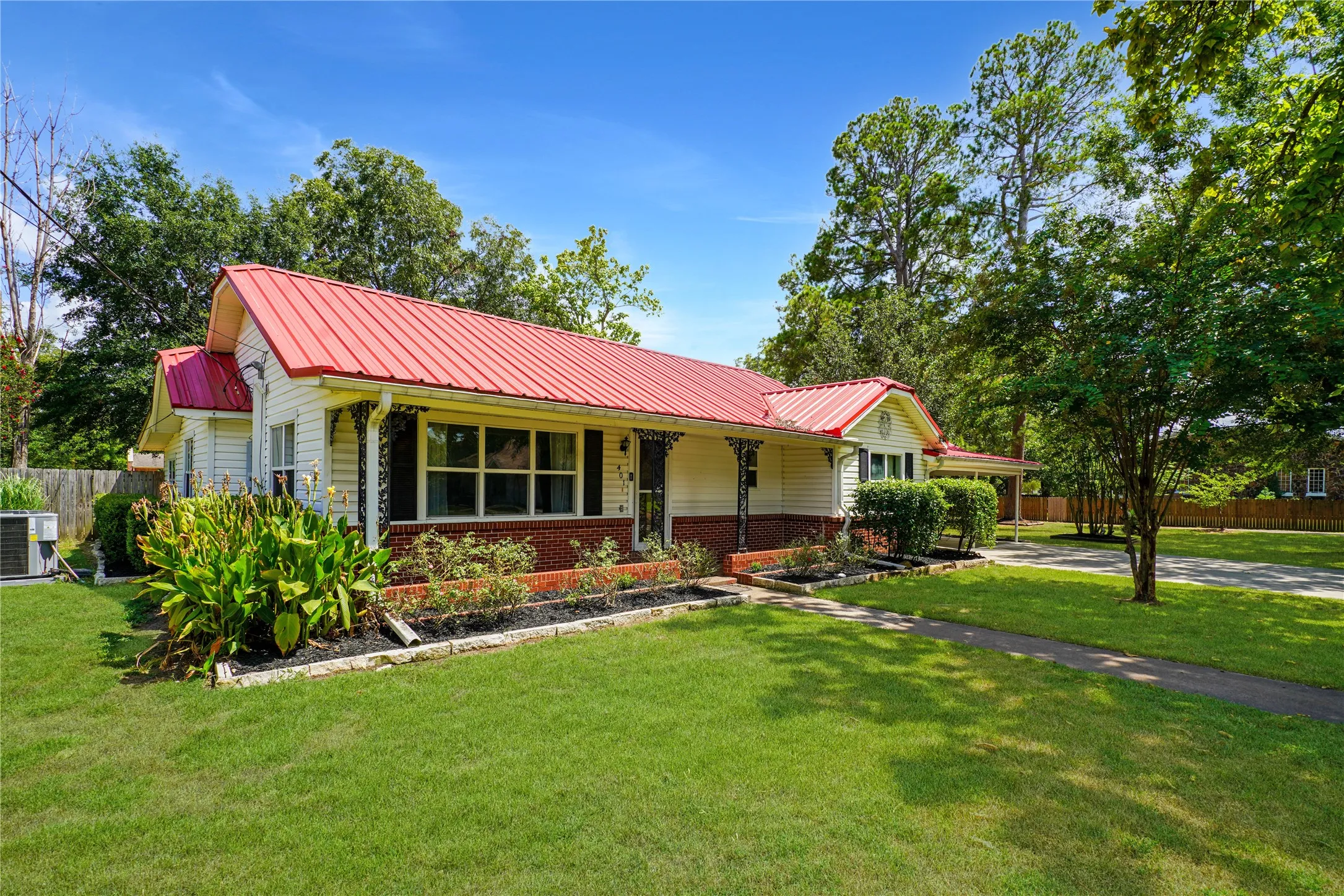 White siding exterior with a red metal roof, brick foundation, and a covered porch with black decorative columns