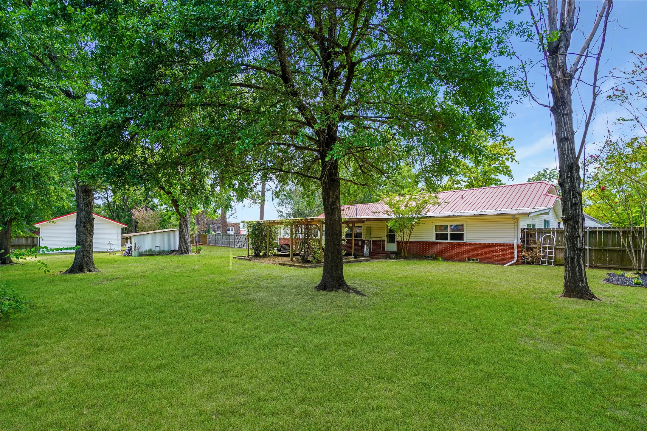 Expansive backyard featuring a manicured lawn, mature trees, and a red metal roof