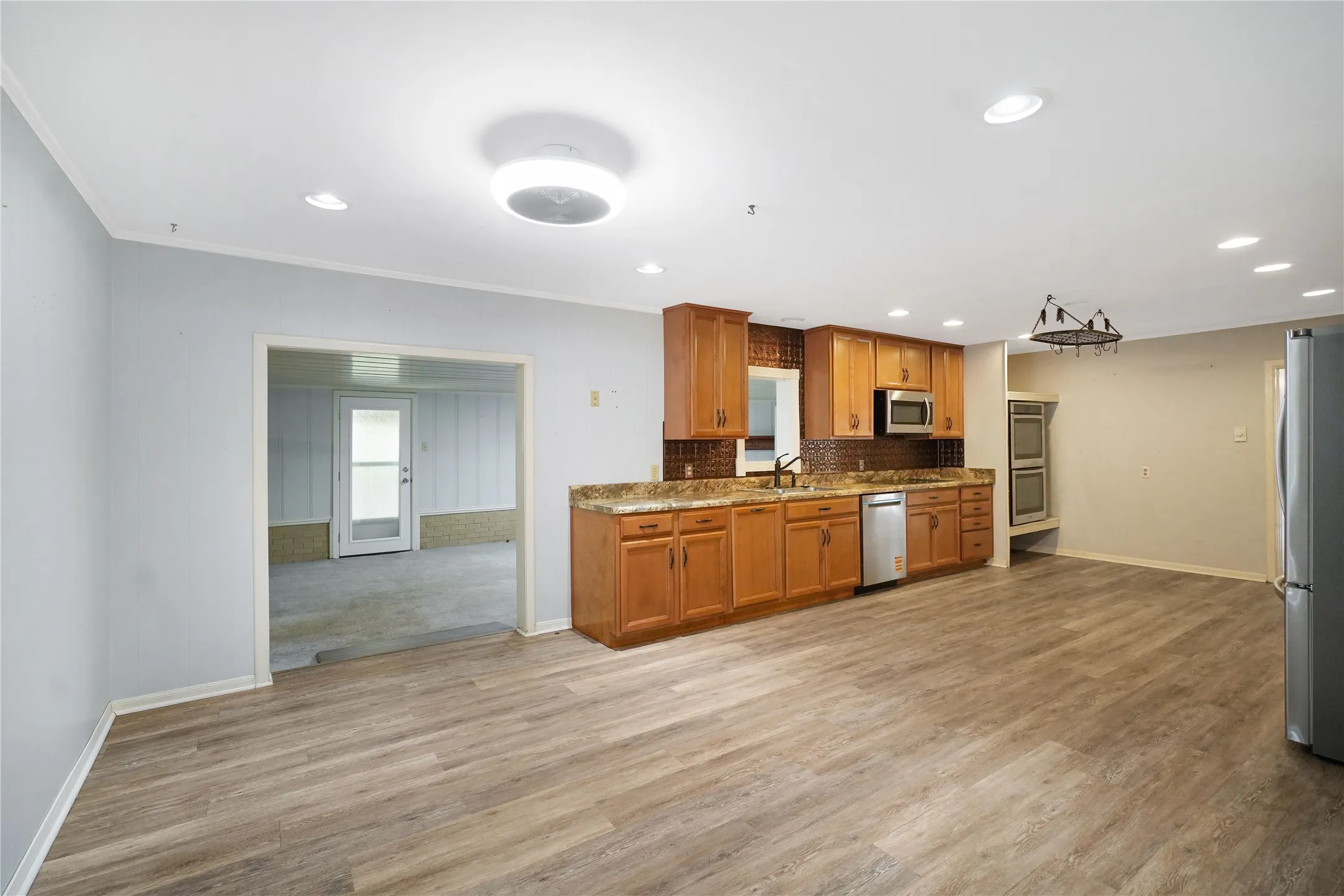 Kitchen area featuring wood-finish flooring, recessed lighting, wood cabinetry, stone countertops, and a tile backsplash
