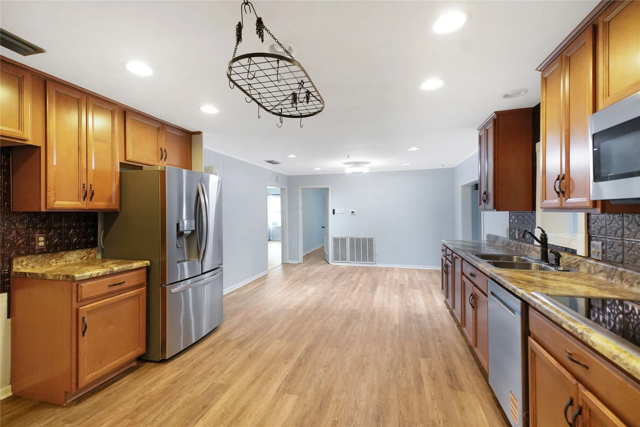 Kitchen featuring wood-finish flooring, recessed lighting, wood cabinetry, stainless steel appliances, and a hammered metal tile backsplash