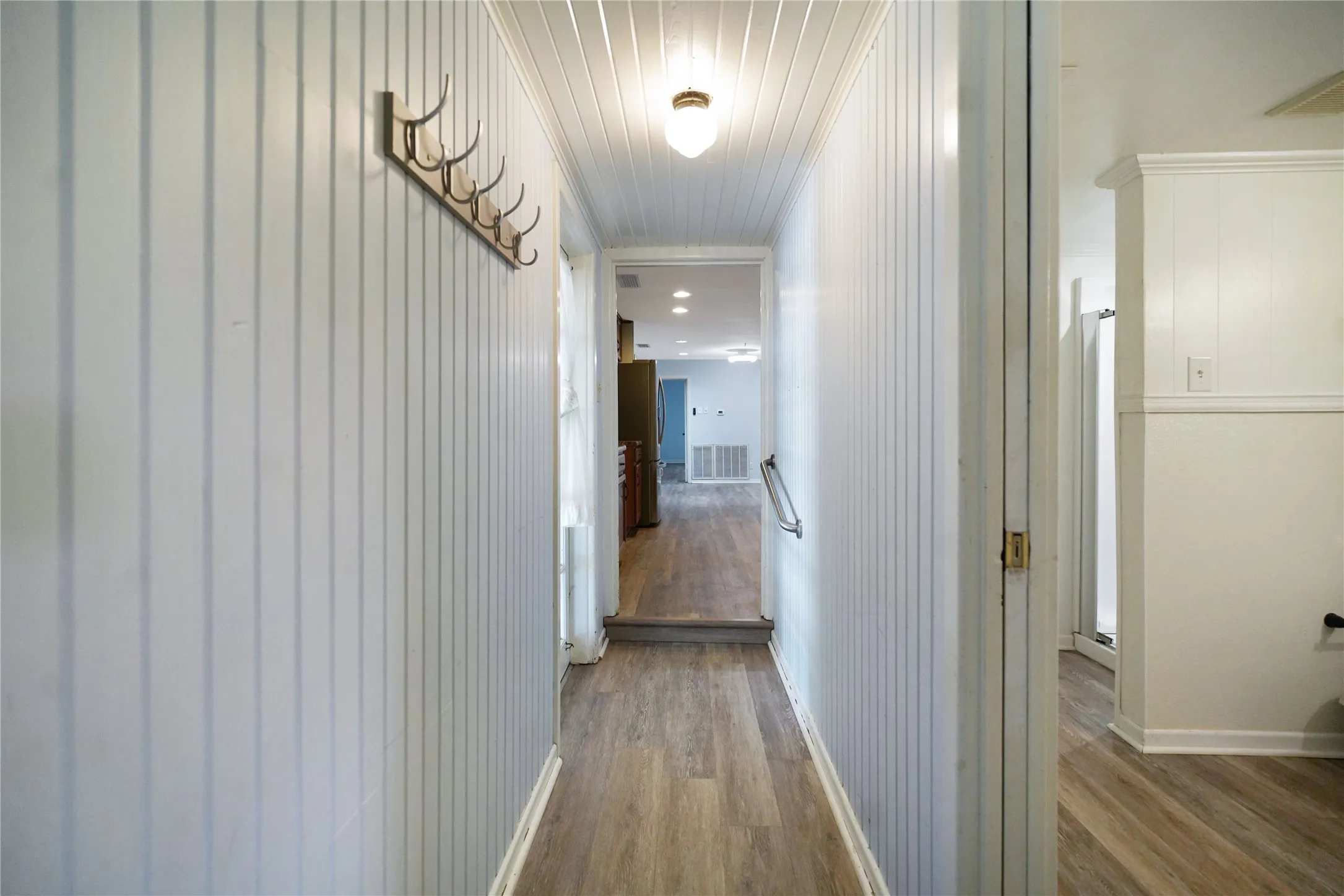 Hallway featuring wood-finish flooring, vertical paneling, and an overhead flush mount light fixture